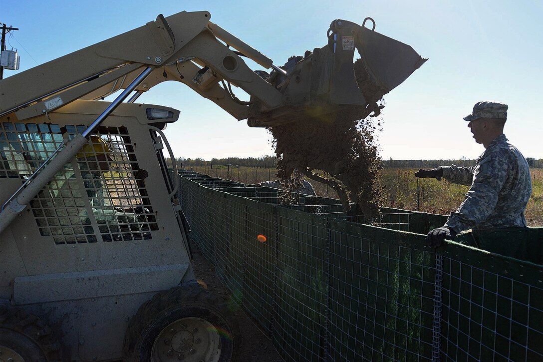 Army Pfc. Dustin Mooney, left, operates a skid loader to fill barriers while Sgt. Craig Smith guides him on Avoca Island, La., Jan. 11, 2016. Mooney is a horizontal construction engineer assigned to the 843rd Engineer Company, 205th Engineer Battalion, 225th Engineer Brigade and Smith is an infantryman assigned to Company B, 2nd Battalion, 156th Infantry Regiment, 256th Infantry Brigade Combat Team. The barrier will be used in the construction of a 2-mile-long levee to prevent backwater flooding from reaching Morgan City and other towns in southern Louisiana due to high river levels. Louisiana National Guard photo by Army Spc. Joshua Barnett