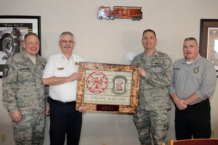 Chief Master Sgt. Eidenschink, 5th Civil Engineer Squadron fire chief (left), C.J. Cavern, former Minot city fire chief, Lt. Col. Bryan Opperman, 5th CES commander and Robyn Roberts, 5th CES deputy fire chief, pose with a going-away gift at Minot Air Force Base, N.D., Jan. 5, 2016. According to Eidenschink, in order to effectively operate in today’s environment, fire chiefs must be able to rely on established partnerships to ensure we have the necessary manpower and equipment when needed to safely mitigate emergencies. (U.S. Air Force photo/Airman 1st Class J.T. Armstrong)