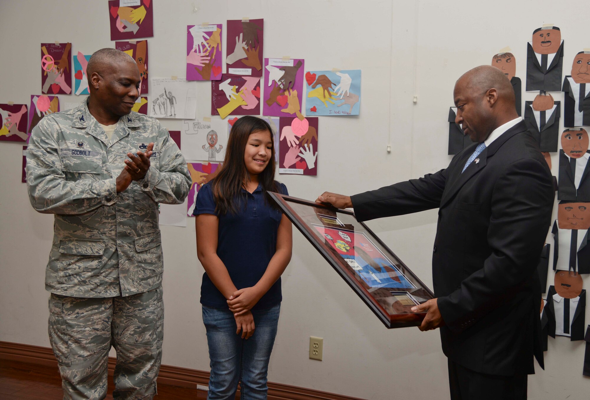 (From Left) Col. Reginald Godbolt, commander of the 6th Maintenance Group, and a Tinker K-8 student present Retired Chief Master Sgt. Derrick Crowley a gift during a Martin Luther King Jr. Special Observance event at MacDill Air Force Base, Fla., Jan. 15, 2015. Crowley served as the guest speaker for the event. (U.S. Air Force photo by Senior Airman Vernon L. Fowler Jr.)