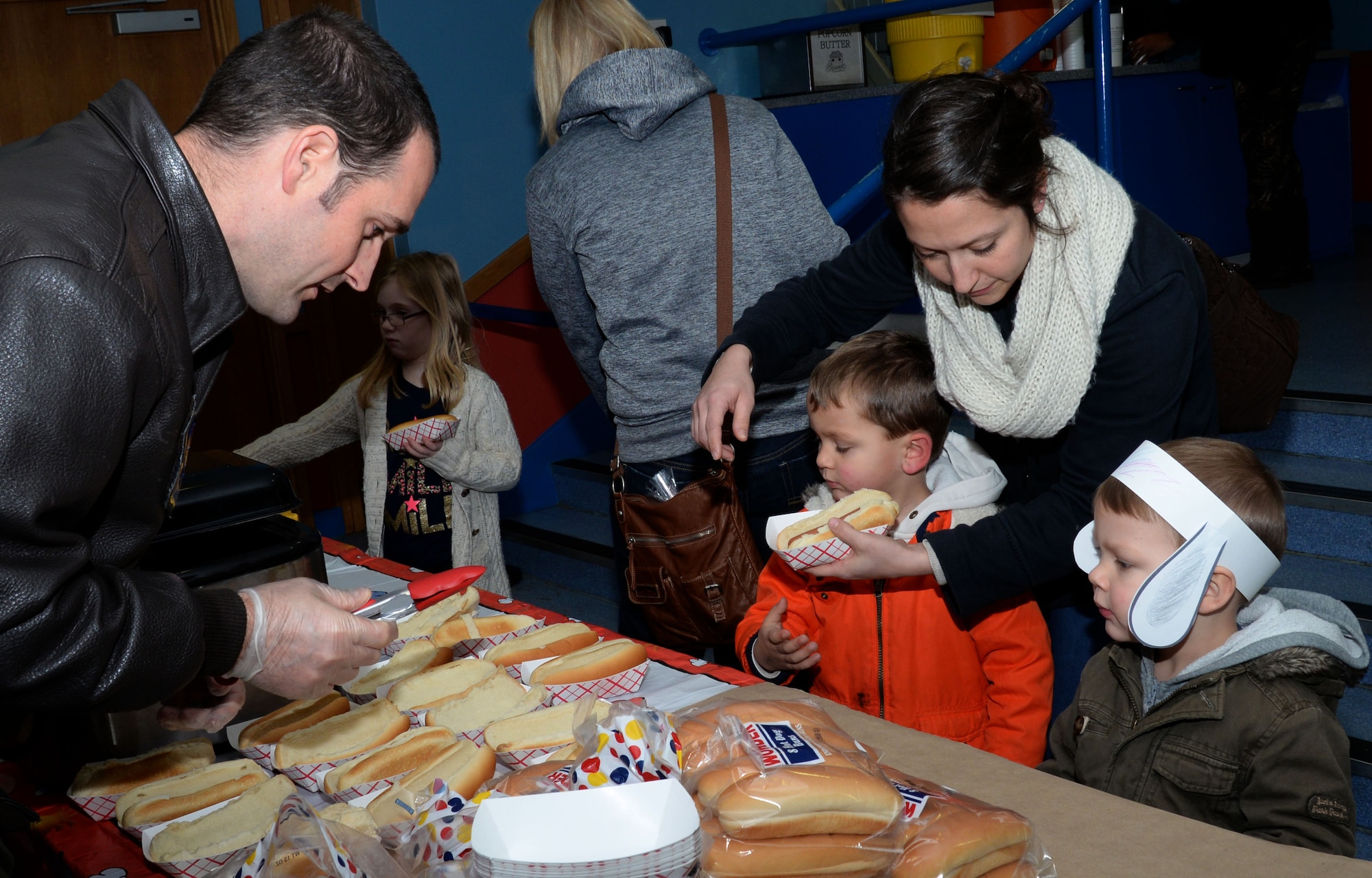 Families grab hot dogs and snacks before viewing The Peanuts Movie during a Hearts Apart event for families of deployed Airmen Jan. 14, 2016, at the base theater on RAF Mildenhall, England. Children were given goodie bags and had the opportunity to make Snoopy ears before the movie. The evening’s events were organized by the Mildenhall Spouses Club to help bring families closer together and develop a sense of community while their loved ones are deployed.  (U.S. Air Force photo by Airman 1st Class Justine Rho/Released)
