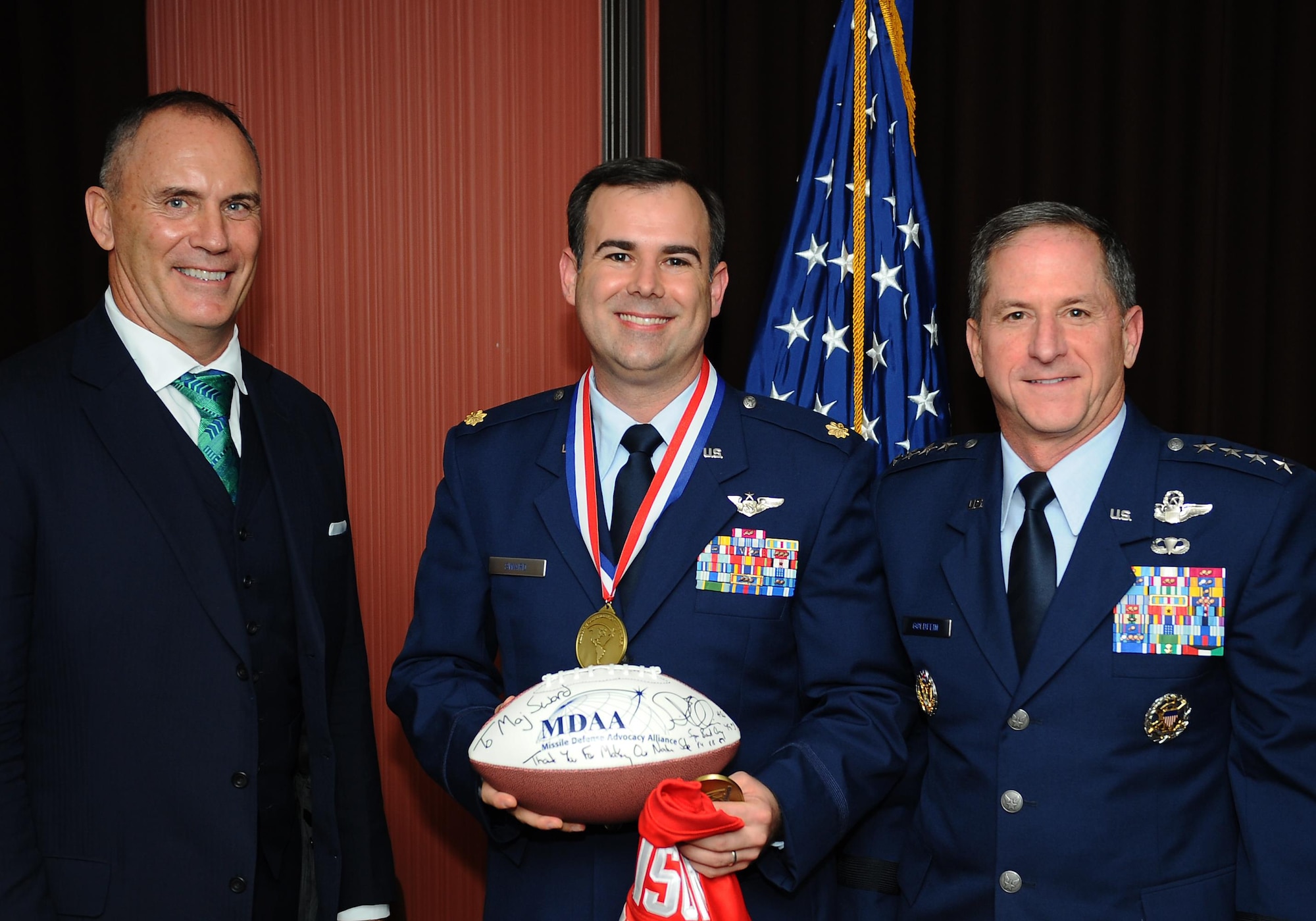 Riki Ellison, the Missile Defense Advocacy Alliance chairman, congratulates MDAA’s 2015 Air Force Defender of the Year award winner, Maj. Michael Sward, a Joint Integrated Air and Missile Defense staff officer, Space and Integrated Air and Missile Defense Division, Operations Directorate, U.S. Pacific Command, as Air Force Vice Chief of Staff Gen. David L. Goldfein looks on during a during a ceremony Jan. 8, 2016, in Alexandria, Va. Sward synchronized non-kinetic activities with active defenses by integrating offensive cyber capabilities into Pacific air and missile defense operations, and coordinated for the analysis of U.S. defenses with high-fidelity, advanced and emerging threat assessments. (U.S. Air Force photo/Tech. Sgt. Bryan Franks)