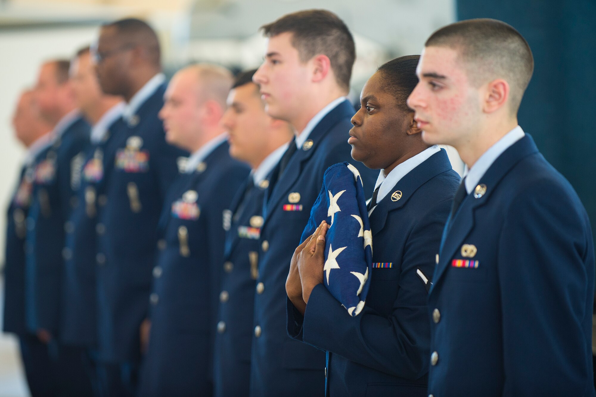 U.S. Air Force Airman Stacy Thomas, 23d Aircraft Maintenance Squadron administrative technician, holds a flag during Chief Master Sgt. Guillermo Castillo’s retirement, Jan. 15, 2016, at Moody Air Force Base, Ga. Passing the flag through the ranks is a military tradition that is performed during retirement ceremonies to symbolize the journey Airmen take from the beginning of their career to the end. (U.S. Air Force photo by Senior Airman Ceaira Tinsley/Released)