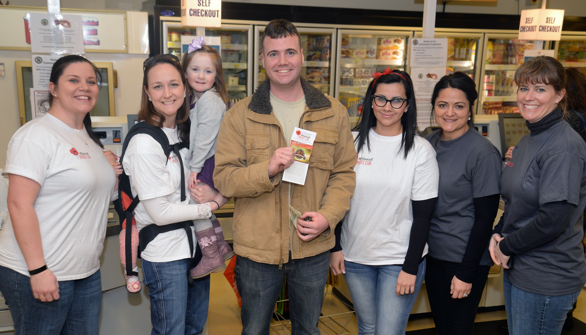 Spouses from the RAF Mildenhall Spouses’ Club pose for a photo with U.S. Air Force Senior Airman Kevin Shaloo, 100th Logistics Readiness Squadron material handling equipment journeyman, Jan. 15, 2016, at the commissary on RAF Mildenhall, England. The spouses handed out 40 gift cards to random personnel between RAF Mildenhall and RAF Lakenheath. Each card contained $25 to spend at the commissary. (U.S. Air Force photo by Senior Airman Christine Halan/Released)