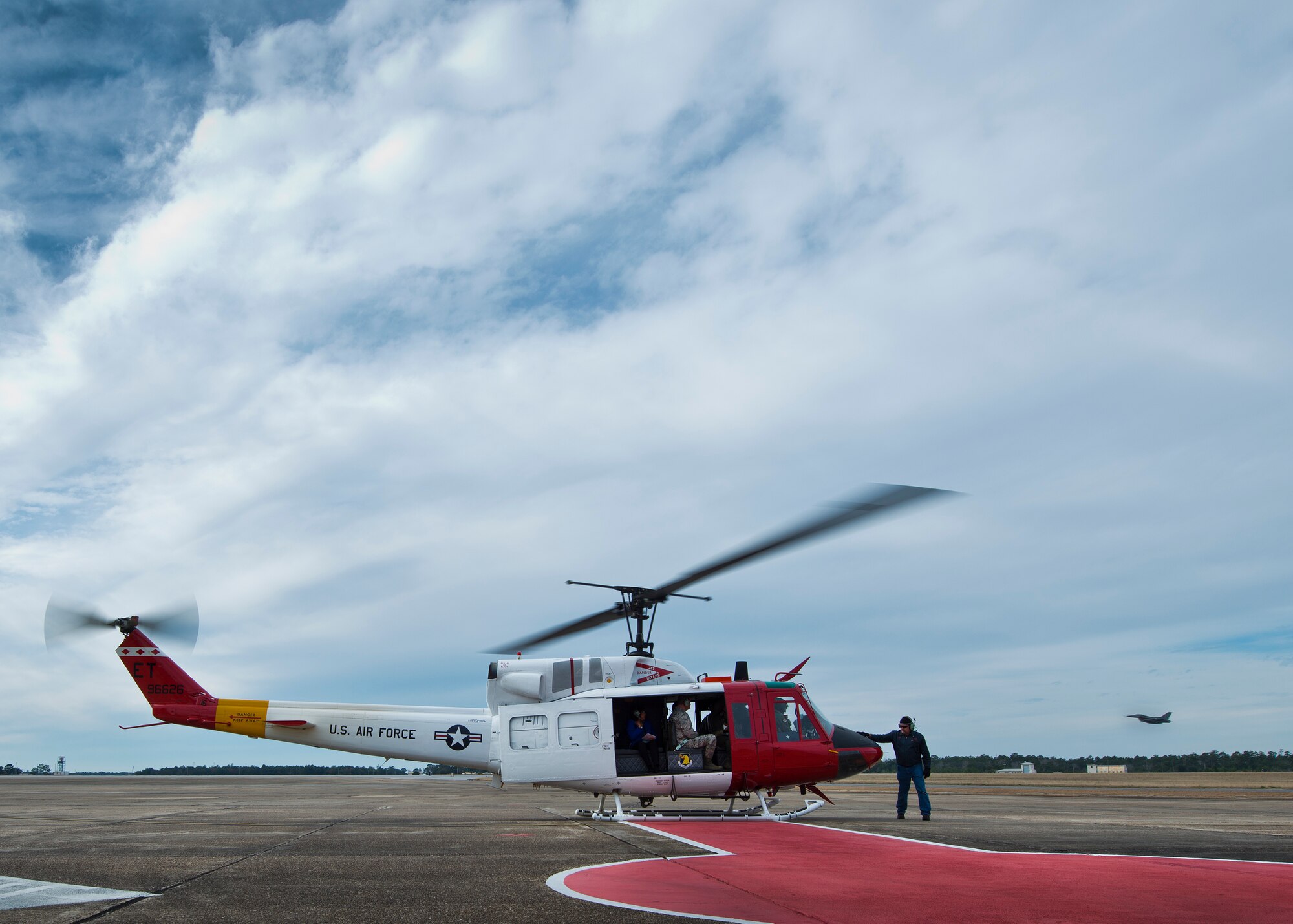 An F-16 Fighting Falcon lifts off from the runway as a UH-1 Huey crew prepares for flight Jan. 14 at Eglin Air Force Base, Fla.  The Huey flight was a touring sortie carrying the Commander-In-Chief’s Installation Excellence Award evaluation team to see Eglin’s range and tenant units.  (U.S. Air Force photo/Samuel King Jr.)