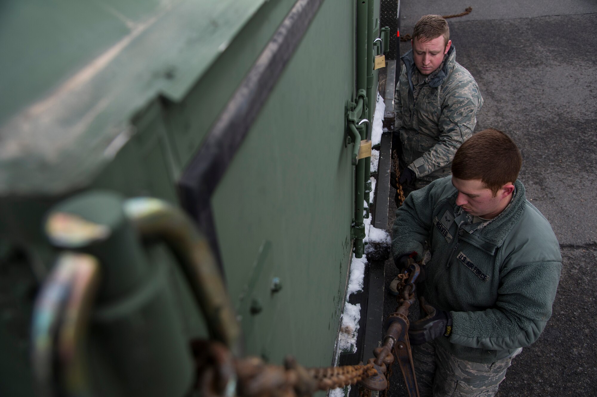 Airman 1st Class Auston R. Reeves and Airman Tucker Gerdes, 92nd Logistics Readiness Squadron vehicle operations journeymen, tighten the chains on a cad bin Jan. 10,  2015, at Fairchild Air Force Base, Wash. Each job vehicle ops works on uses a different vehicle. For transporting cad bins and other equipment, they have tractor trailer trucks with several different styles of trailers for towing. (U.S. Air Force photo/Airman 1st Class Nick J. Daniello )
