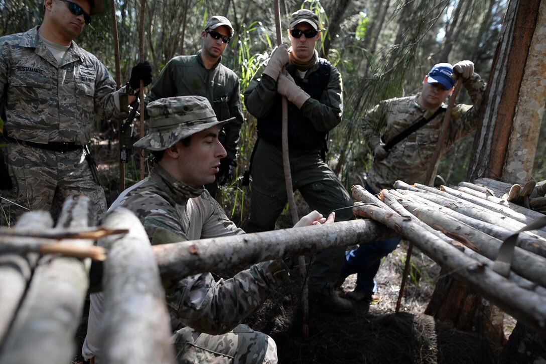 Air Force Staff Sgt. Brian Alfano, foreground, shows participants how to construct a shelter during a combat and water survival training course on Homestead Air Reserve Base, Fla., Jan. 18, 2016. Alfano is a survival, evasion, resistance, and escape instructor assigned to the 103rd Rescue Squadron. During the training, aircrew members gained refresher training on using their emergency radios, tactical movements through difficult terrain, how to build shelters, ways to build fires, and methods for evading the enemy. New York Air National Guard photo by Staff Sgt. Christopher S. Muncy