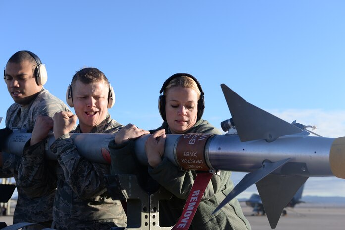 Senior Airman John Luke Wright, Staff Sgt. Eric McClendon and Senior Airman Kelly Sifers, weapons technician specialists from the 57th Aircraft Maintenance Squadron, Viper AMU, pick up munition during a weapons load competition at Nellis Air Force Base, Nev., Jan. 8, 2016. Weapons load competitions are done quarterly. (U.S. Air Force photo by Airman 1st Class Nathan C. Byrnes)