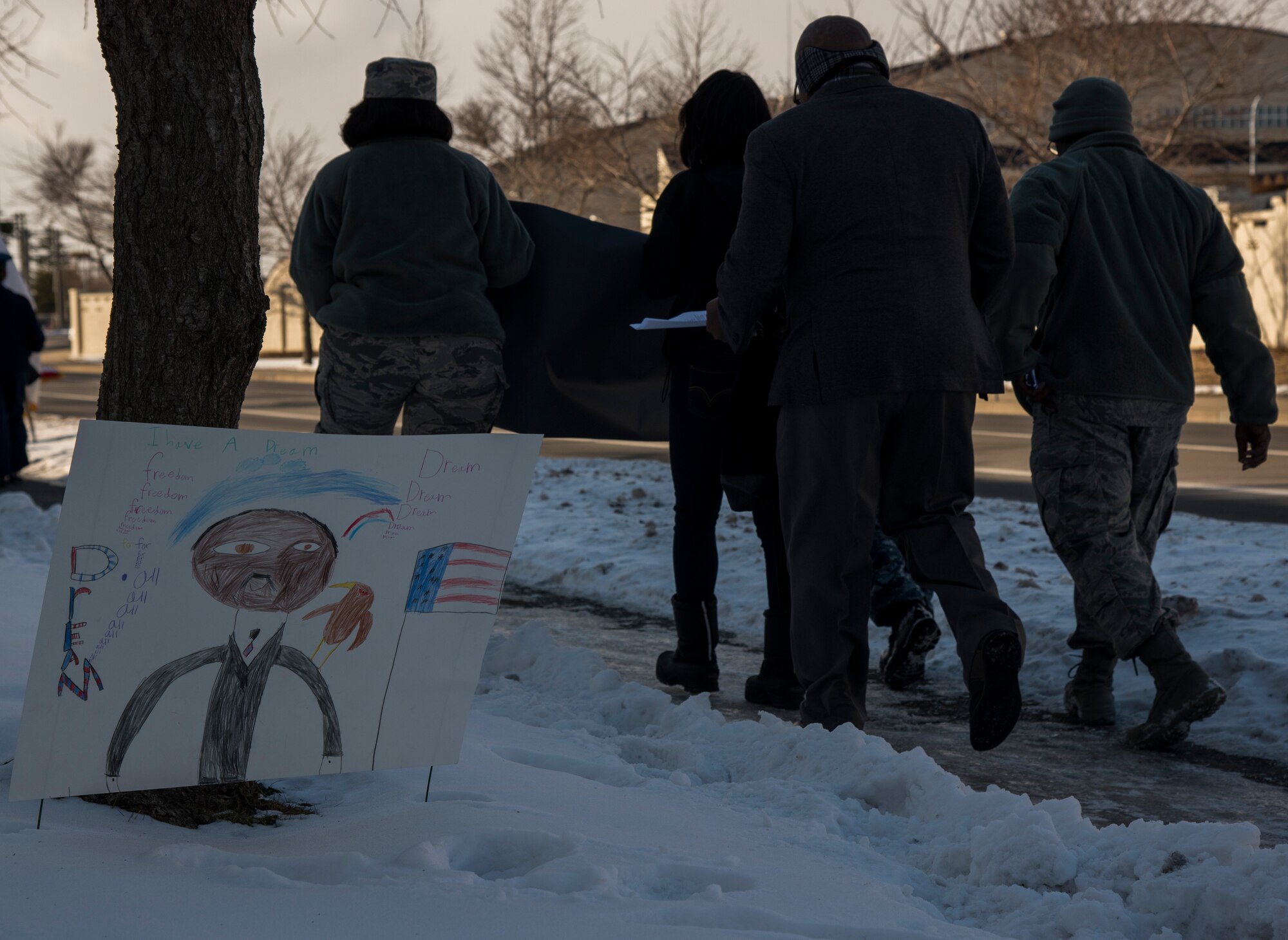 A Martin Luther King, Jr. poster is displayed in the snow while marchers pass by at Misawa Air Base, Japan, Jan. 15, 2016. In honor of MLK Day, students from Edgren Middle School made posters to place around Misawa. Martin Luther King, Jr. Day is an American federal holiday marking the birthday of MLK; It is observed on the third Monday of January each year, which is around King's birthday, January 15. (U.S. Air Force photos by Senior Airman Brittany A. Chase)