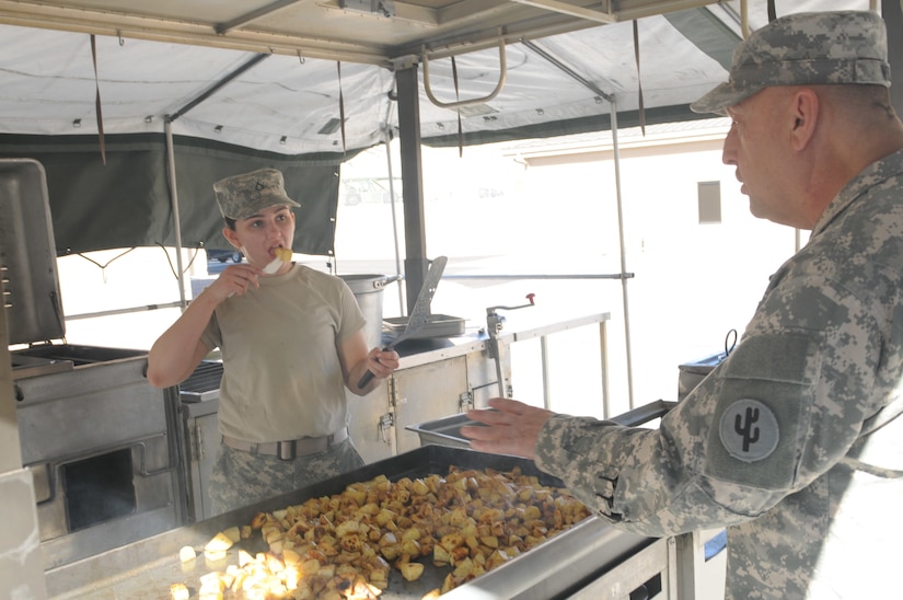Pfc. Genephere Mata, 650th Regional Support Group, listens to instructions from Chief Warrant Officer 2 Danny Wolf, 103rd Sustainment Command (Expeditionary) and coach of the Army Reserve Culinary Arts Team, as she tests the hash browns while training on a mobile kitchen trailer.