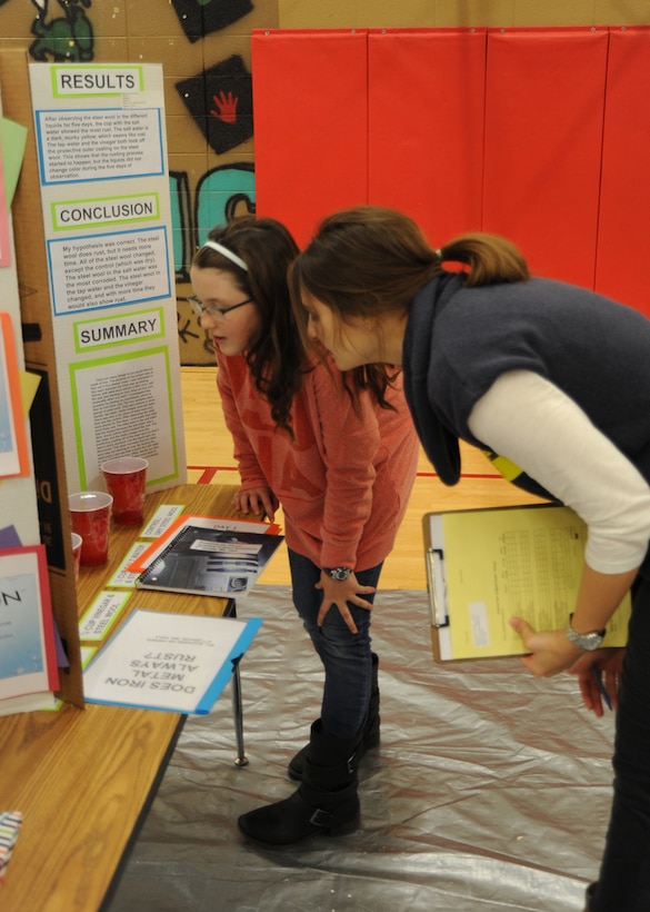Gina Gill, a project manager with the Energy Saving Performance Contract program, bends down to hear Suzanne DeVisser’s explanation of her fifth grade science fair presentation on “Does Iron Metal Always Rust?” during the Challenger Elementary School Science Fair Jan. 20. Visser received an Honorable Mention for the science fair’s physical category. 