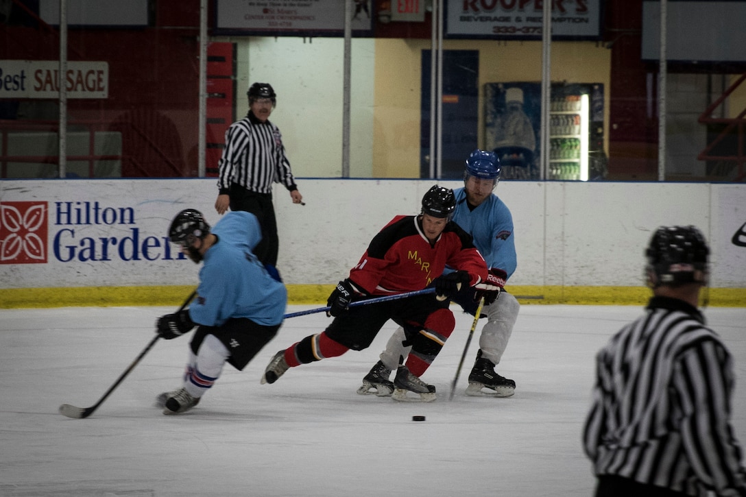 A Marine with the Marine Corps Ice Hockey Team works a puck past a defensive player during The Maine Event, Battle on Ice hockey tournament, Jan. 15. The team is made up of 40 players from across the Marine Corps, 15 of whom are playing in the tournament. This is the first time the team has played together and is aiming to create a Marine Corps-recognized All-Marine Ice Hockey Team.