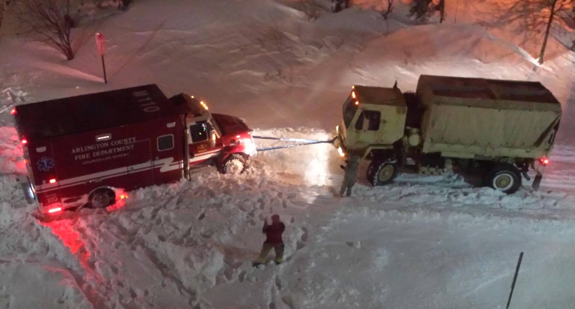 Two Soldiers from the Virginia National Guard's Fredericksburg-based Company F, 429th Brigade Support Battalion, 116th Infantry Brigade Combat Team use their medium tactical truck to assist an Arlington County Fire Department ambulance stuck in heavy snow Jan. 23, 2016, in Rosslyn, Virginia. 