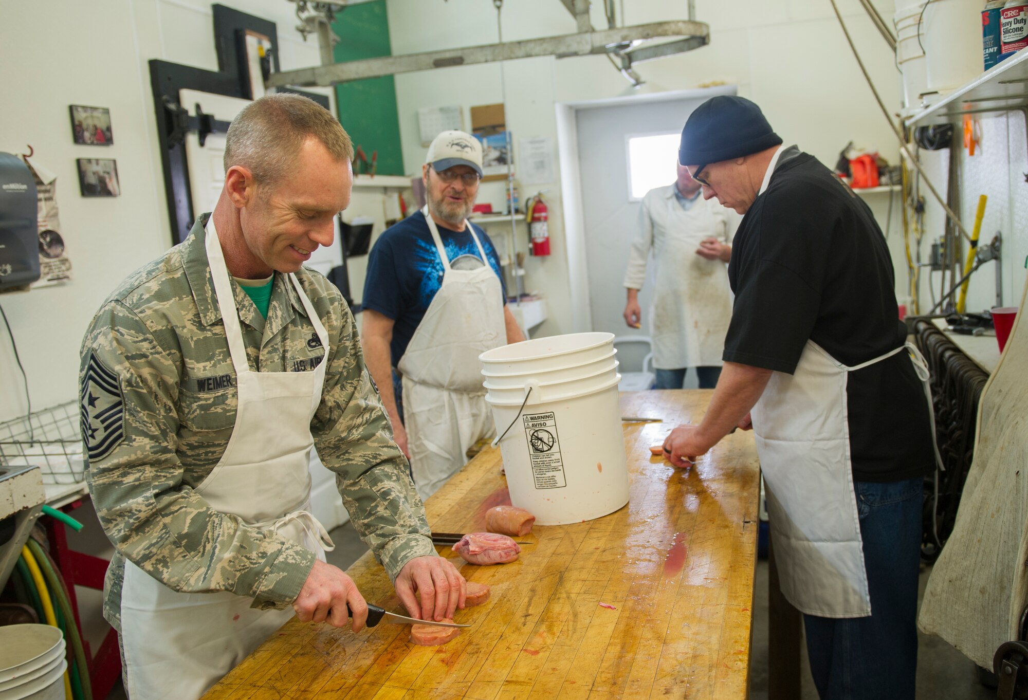 Chief Master Sgt. Geoff Weimer, 5th Bomb Wing command chief, and community members cut meat at the Sportsmen Feed cut-up event at Bloms’ Locker & Processing in Minot, N.D., Jan. 22, 2015. The cut-up event preceeds the Sportsmen Feed event on base, which features an array of wild game. (U.S. Air Force photo/Senior Airman Apryl Hall)