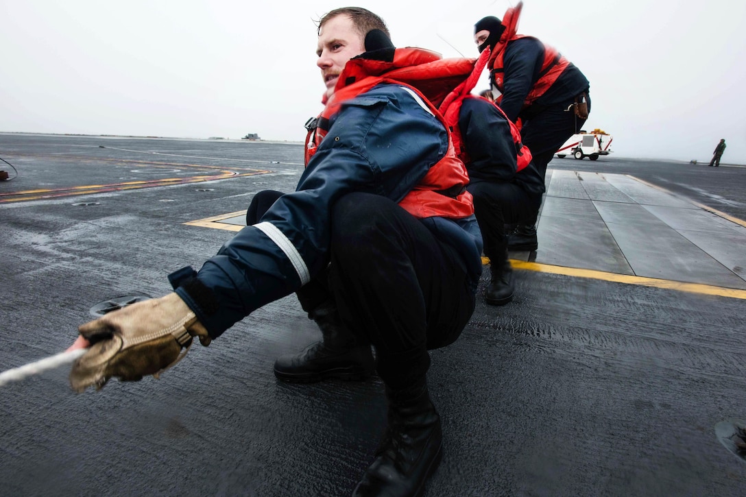 Navy Seaman David Schneider, foreground, heaves on the phone and distance line on the flight deck of USS John C. Stennis during a replenishment at sea in the Pacific Ocean, Jan. 18, 2016. U.S. Navy photo by Petty Officer 3rd Class Kenneth Rodriguez Santiago