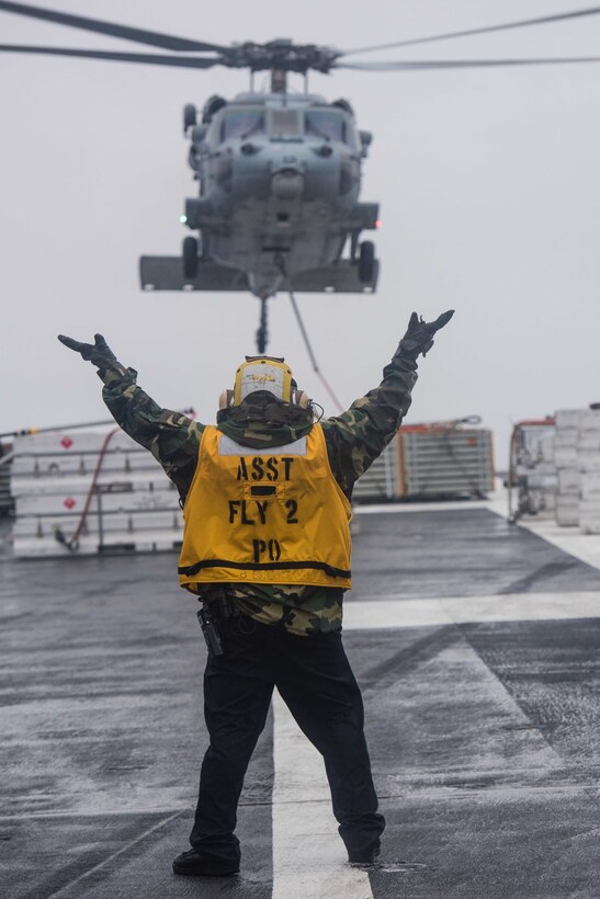 Navy Petty Officer 2nd Class Randy Morta directs a Navy MH-60S Sea Hawk helicopter assigned to Helicopter Sea Combat Squadron 14 as it lands on the flight deck of USS John C. Stennis during a replenishment at sea with USNS Rainier in the Pacific Ocean, Jan. 18, 2016. Morta is an aviation boatswain's mate handling. U.S. Navy photo by Petty Officer 3rd Class Kenneth Rodriguez Santiago