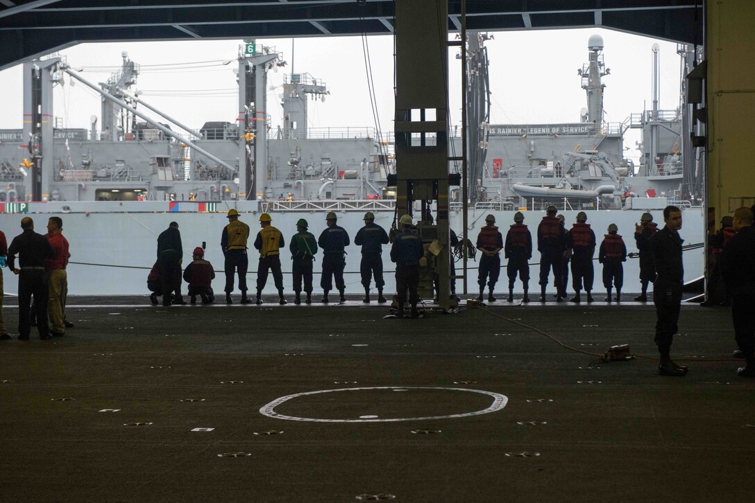Sailors in the hangar bay of USS John C. Stennis prepare for a replenishment at sea with USNS Rainier, background, in the Pacific Ocean, Jan. 18, 2016. U.S. Navy photo by Seaman Tomas Compian