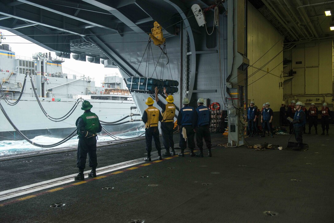 U.S. sailors in the hangar bay of USS John C. Stennis receive cargo from the USNS Rainier during a replenishment at sea in the Pacific Ocean, Jan. 18, 2016. U.S. Navy photo by Seaman Tomas Compian