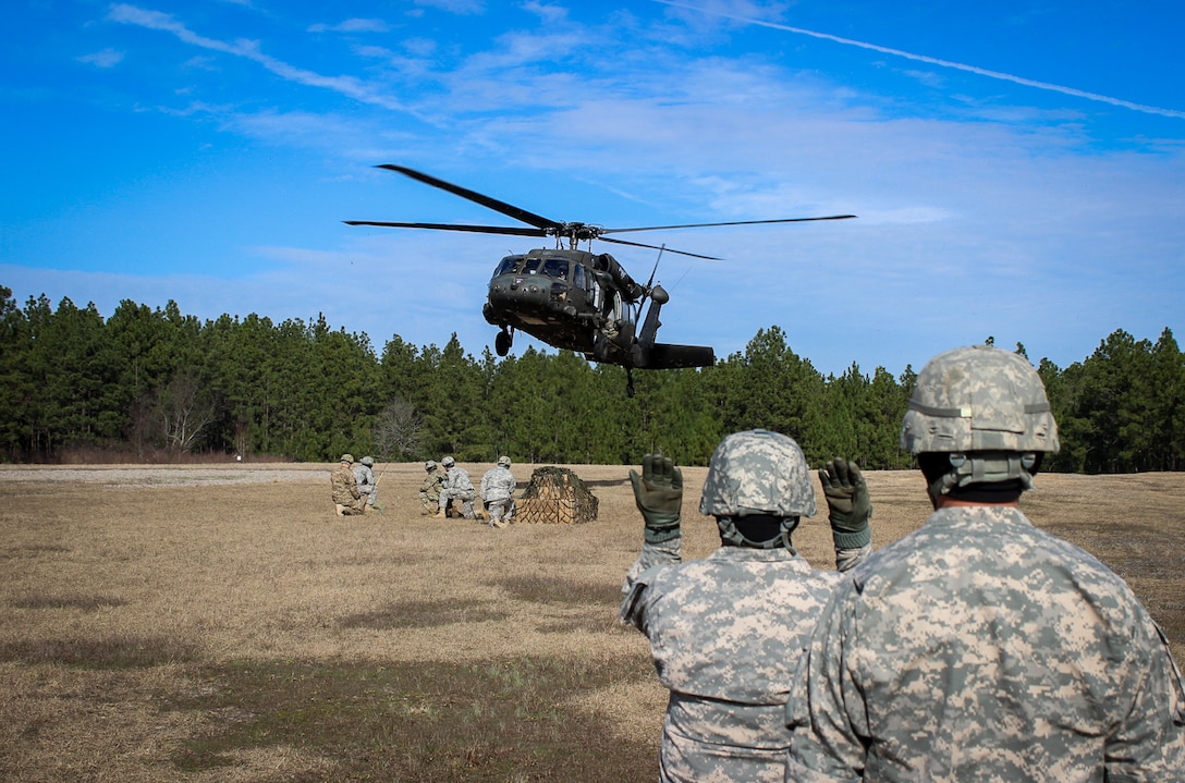 A paratrooper uses hand signals to guide a UH-60 Black Hawk helicopter while team members wait with a cargo net of supplies during slingload operations training on Fort Bragg, N.C., Jan. 20, 2016. The paratroopers are assigned to the 82nd Airborne Division’s 73rd Cavalry Regiment, 1st Brigade Combat Team. The training enhances the paratroopers' ability to maintain a logistical advantage. Army photo by Sgt. Chad Haling