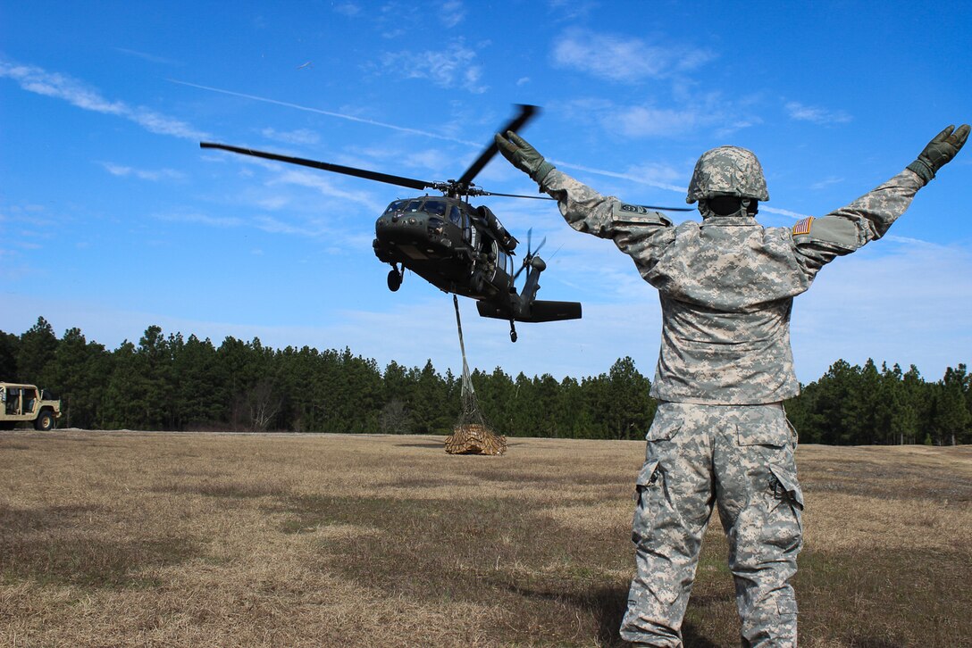 A paratrooper signals the UH-60 Black Hawk helicopter pilots to take off with a cargo net of supplies during slingload training on Fort Bragg, N.C., Jan. 20, 2016. Army photo by Sgt. Chad Haling    