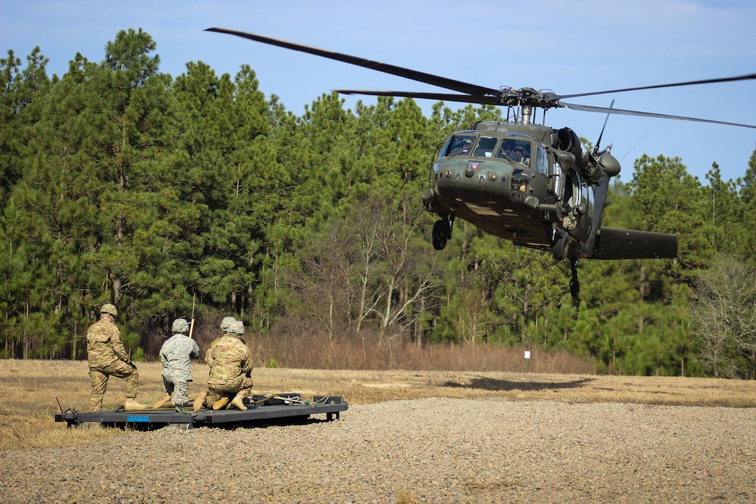 An Army crew chief checks for clearance while paratroopers prepare to connect a flat rack to a UH-60 Black Hawk helicopter during slingload training on Fort Bragg, N.C., Jan. 20, 2016. The connection process requires perfect communication between air and ground crew, via hand and arm signals. Army photo by Sgt. Chad Haling