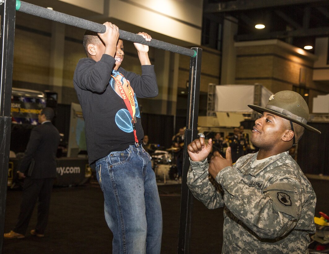 Army Reserve drill sergeant, Staff Sergeant Brian Johnson, Task Force Marshall, 108th Training Command (IET), encourages a young fan to do one more pull-up at Fan Fest during the 2015 CIAA basketball tournament held annually in Charlotte, N.C. Johnson was on hand to tout the benefits and opportunities of military service by way of the Army Reserve. (U.S. Army Photo by Sgt. 1st Class Brian Hamilton)