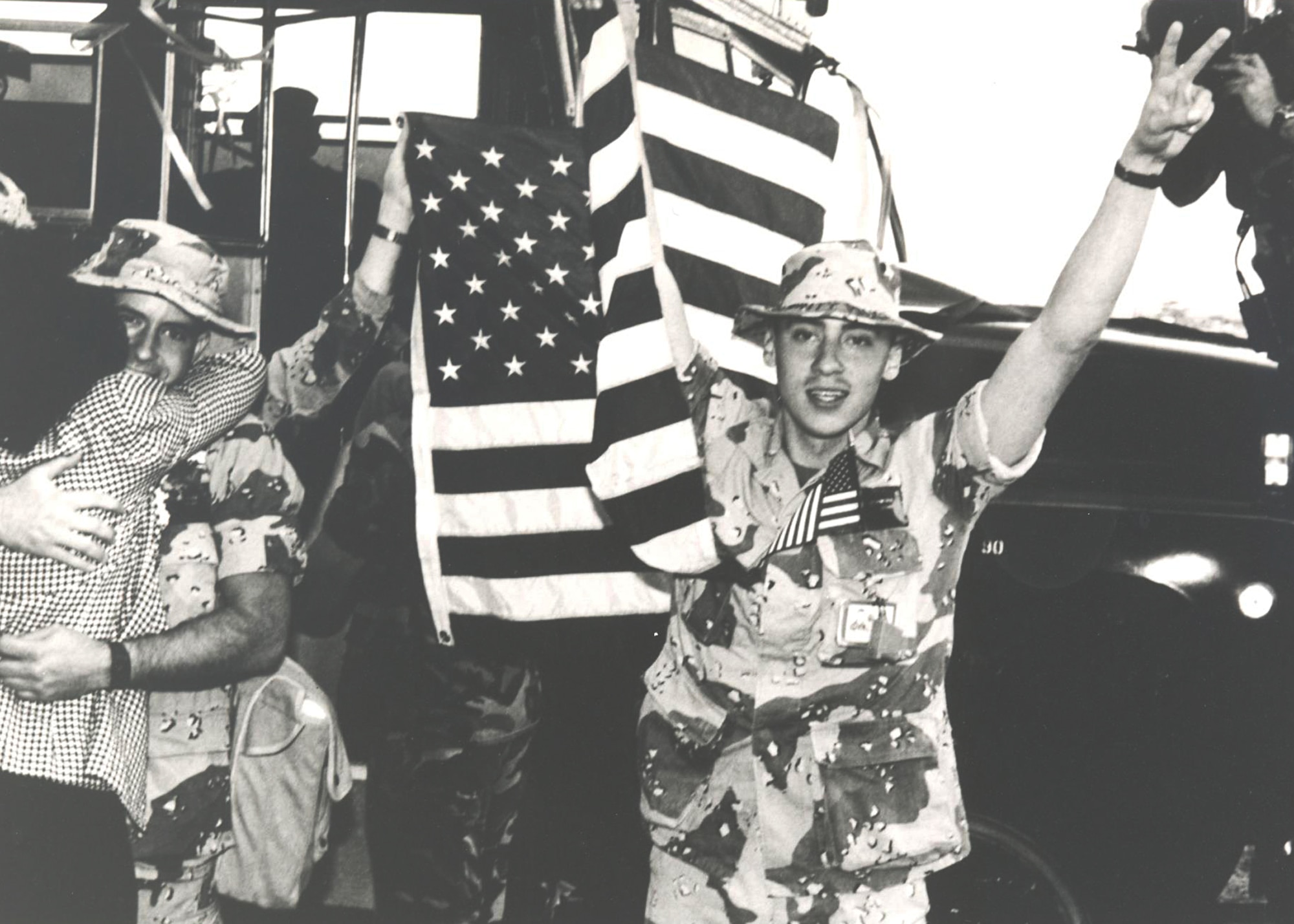 SrA Kevin D. Schwinn waves the American flag and flashes a victorysign following his return from Desert Storm with other members of the15th Security Police Squadron. At left, getting a big hug, is AlCPatrick S. Waters. (Courtesy Photo)