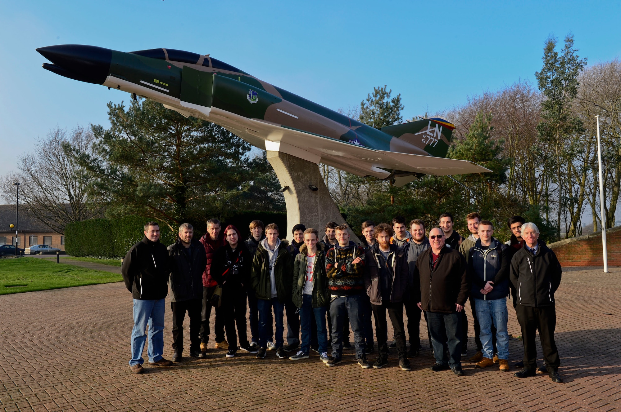 Suffolk New College students take a group photo at the outdoor air museum at Royal Air Force Lakenheath, England, Jan. 20, 2016. The 24 U.K. diagnostic and recertification students spent the afternoon touring the vehicle maintenance section of the 48th Logistics Readiness Squadron to see what it would be like to work on American cars. (U.S. Air Force photo by Senior Airman Nigel Sandridge/ Released)
