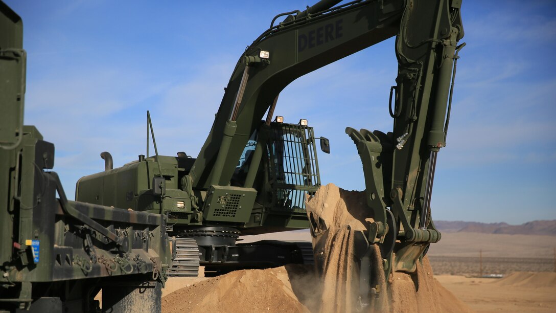Staff Sgt. John Vasquez, heavy equipment operations chief, Marine Wing Support Squadron 374, scoops sand with a John Deere 250 GR Hydraulic Excavator near the Strategic Expeditionary Landing Field, Jan. 22, 2016. Marines with MWSS-374 and MWSS-371 attended the two-week maintainer and operator courses, Jan. 11-22.