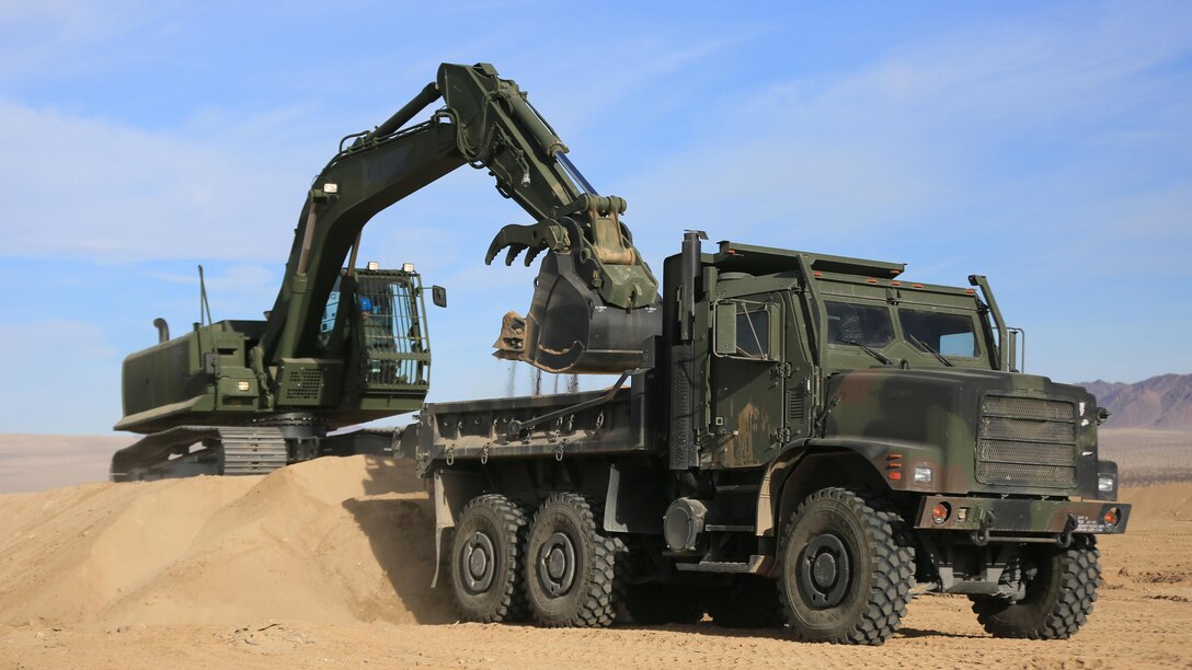 Staff Sgt. John Vasquez, heavy equipment operations chief, Marine Wing Support Squadron 374, scoops sand into a Medium Tactical Vehicle Replacement with a John Deere 250 GR Hydraulic Excavator near the Strategic Expeditionary Landing Field, Jan. 22, 2016. This is the first time MWSS-374 is using this excavator aboard the Combat Center and it is capable of utilizing interchangeable attachments to fulfill critical engineering missions.