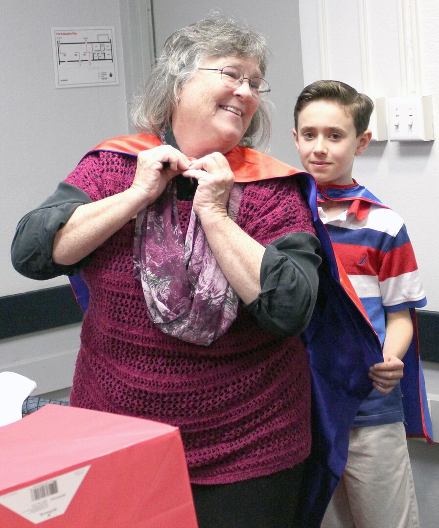 Fort Sam Houston Elementary fourth-grade student Aedan Borgkvist presents Jeanne Warren, Fort Sam Houston Independent School District board secretary, with her superhero cape during School Board Recognition month.