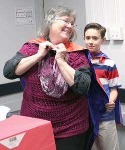 Fort Sam Houston Elementary fourth-grade student Aedan Borgkvist presents Jeanne Warren, Fort Sam Houston Independent School District board secretary, with her superhero cape during School Board Recognition month.