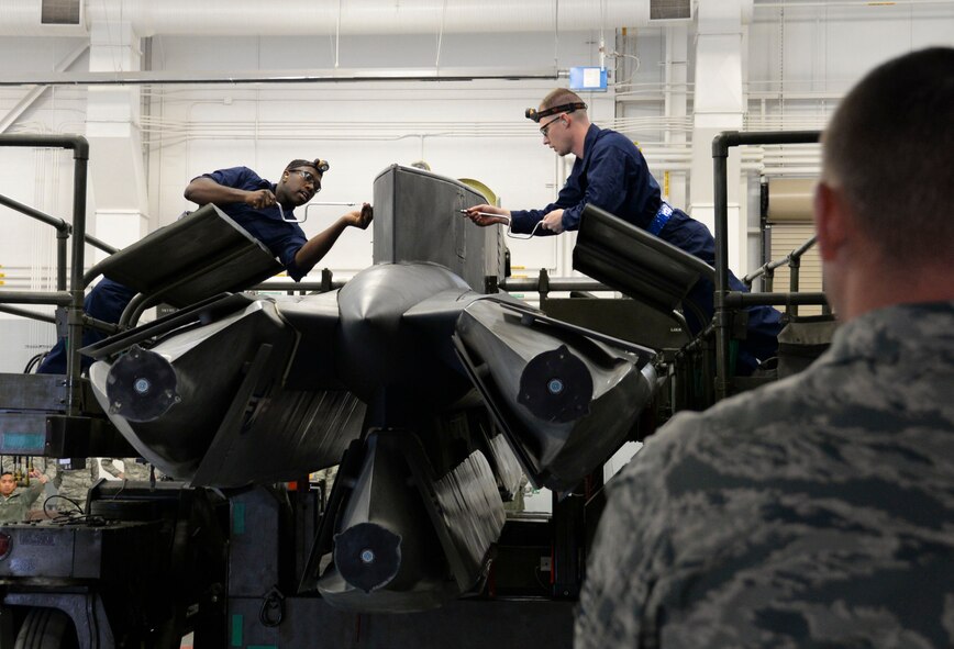 A member of 2nd Maintenance Group loading standardization crew observes weapons load crew team members from the 20th Aircraft Maintenance Unit while they open access panels during the weapons load finals at Barksdale Air Force Base, La., Jan. 21, 2016. The Airmen loaded a munition onto the pylon during their competition performance. (U.S. Air Force photo by Senior Airman Amanda Morris)