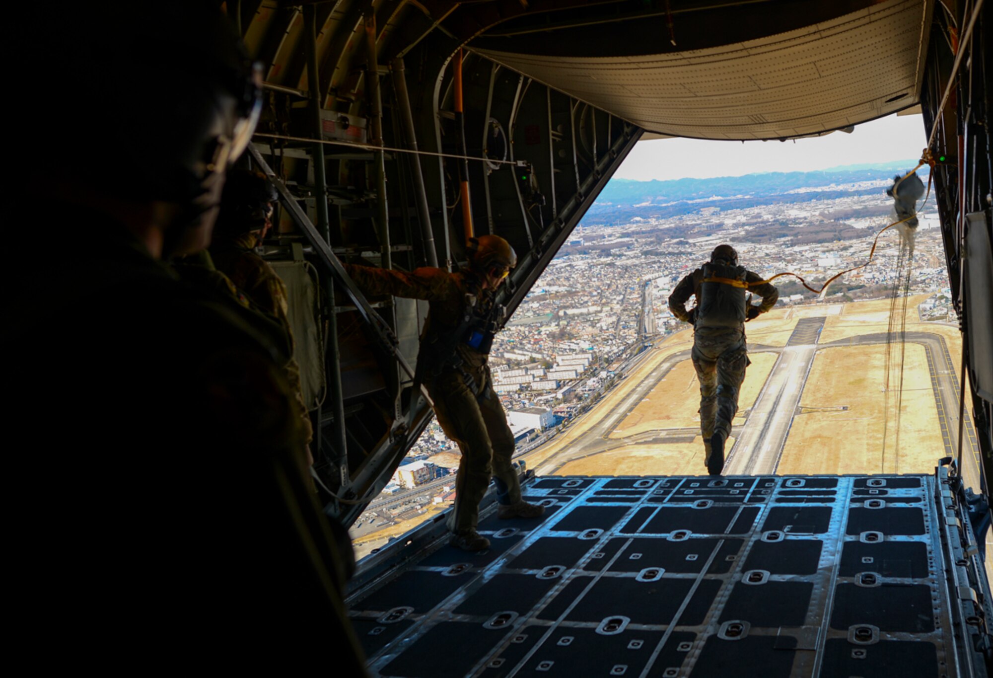 Senior Airman Andrew Fox, 36th Airlift Squadron instructor loadmaster with C-130 Hercules, supervises a personnel drop over Yokota Air Base, Japan Jan. 25, 2016. Loadmasters are responsible for ensuring that aircraft cargo and passengers are transported safely and in a timely manner, which involves preparing rigging inside the aircraft and performing checks before and during the flight to ensure the safety of personnel and equipment. (U.S. Air Force photo by Airman 1st Class Elizabeth Baker/Released)