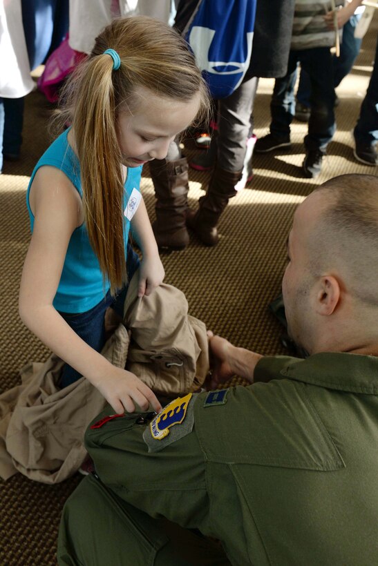 Capt. Hansel Rabell, 28th Operations Support Squadron chief of wing scheduling, helps Capri Poile try on a flight suit during the 2016 Aviation Day at the Discovery Center in Pierre, S.D., Jan. 27, 2016.  The goal of the event was to teach children about aviation while providing a fun environment for them to learn. (U.S. Air Force photo by Senior Airman Rebecca Imwalle/Released)