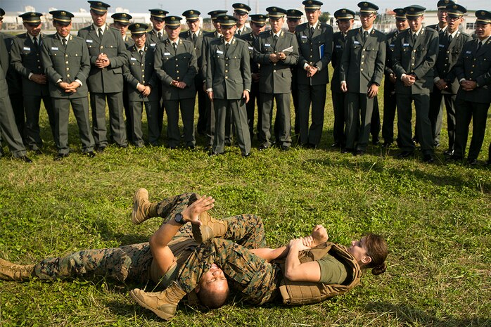 First Lt. Melissa Cooling demonstrates a Marine Corps Martial Arts Program arm bar to Japan Ground Self-Defense Force officer candidates on Camp Kinser, Okinawa, Japan, Jan. 15. Three hundred and sixty officer candidates visited Combat Logistics Regiment 35 to complete joint and combined operation requirements. The cadets watched Marine Corps Martial Art Program demonstrations, learned the capabilities of various machine guns the Marine Corps uses, and observed a static display of motor transportation vehicles. Cooling, from Southbury, Connecticut, is the current operations officer with CLR-35, 3rd Marine Logistics Group, III Marine Expeditionary Force. (U.S. Marine Corps photo by Cpl. Robert Williams Jr./Released)