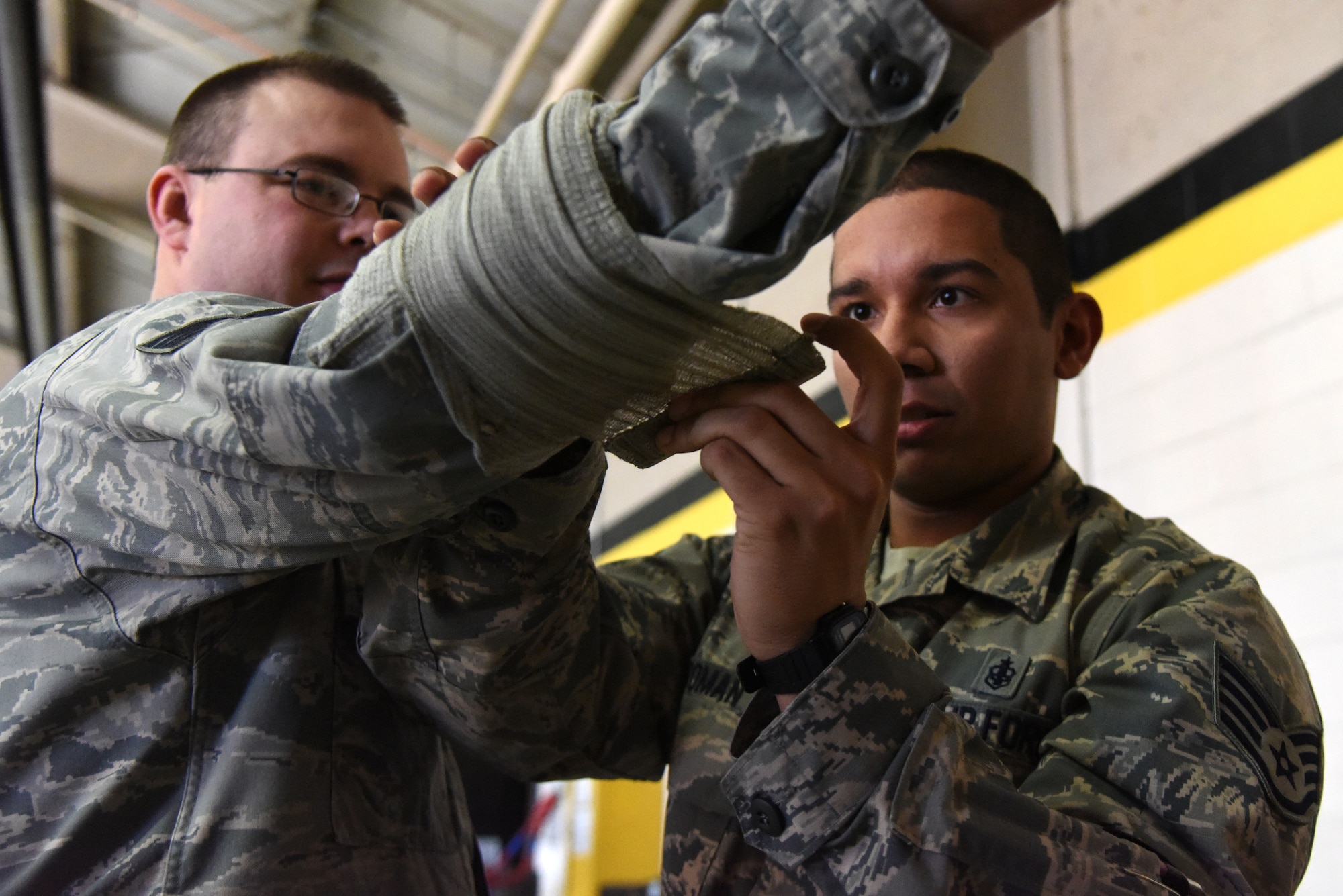 Staff Sgt. Kevin Roman, 4th Aerospace Medicine Squadron public health technician, demonstrates bandaging the arm of Tech. Sgt. Robert Catron, 4th Operations Support Squadron weather craftsman, Jan. 29, 2016, at Seymour Johnson Air Force Base, North Carolina. Both Roman and Catron completed stations on self-aid buddy care, unexploded ordnance identification and chemical decontamination during exercise Coronet Warrior 16-01. (U.S. Air Force photo/Staff Sgt. Chuck Broadway)