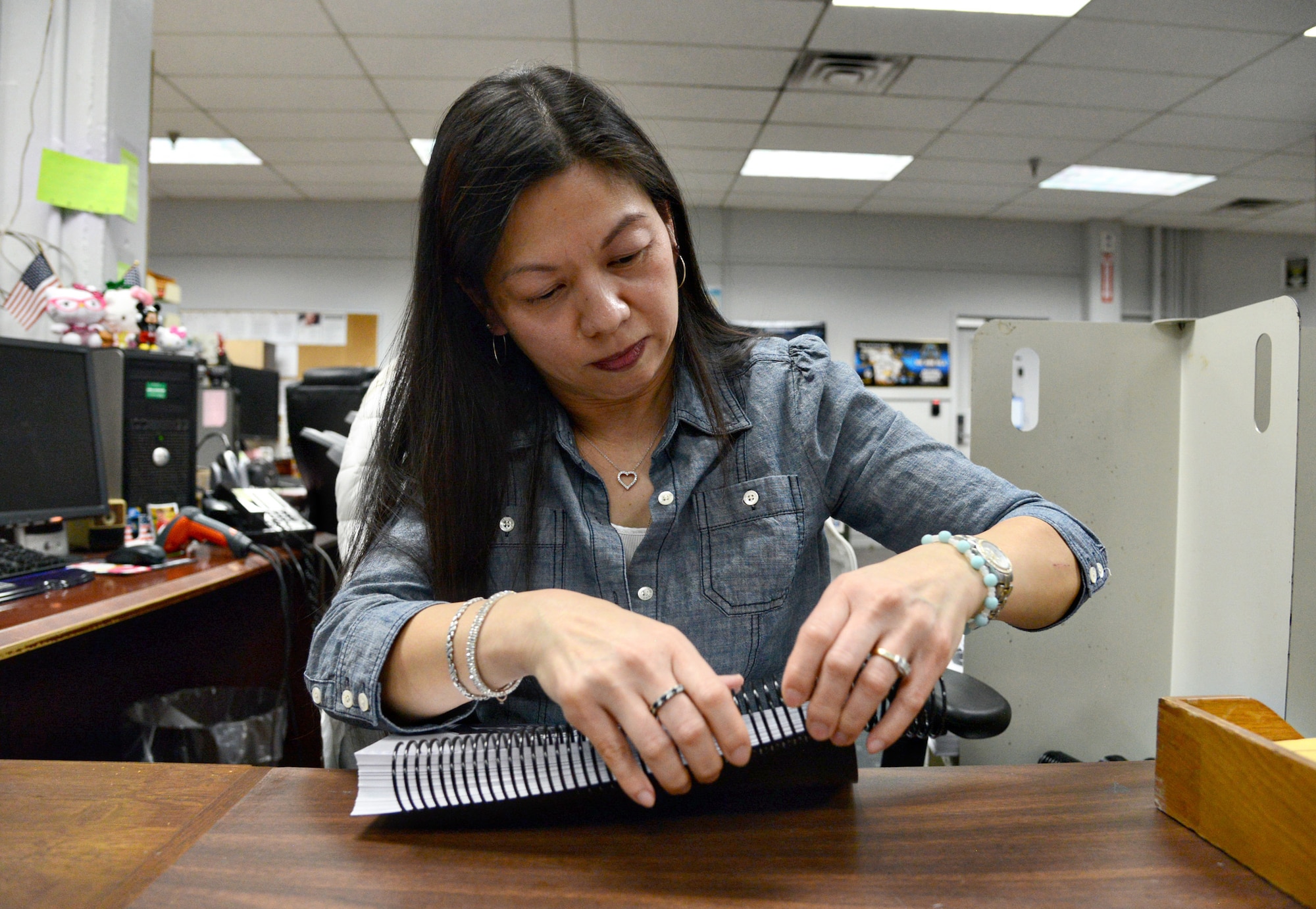 Linh Hastings, an electronic document systems technician with DLA Document Services, hand-feeds spiral binding into a book.  (Air Force photo by Kelly White/Released)