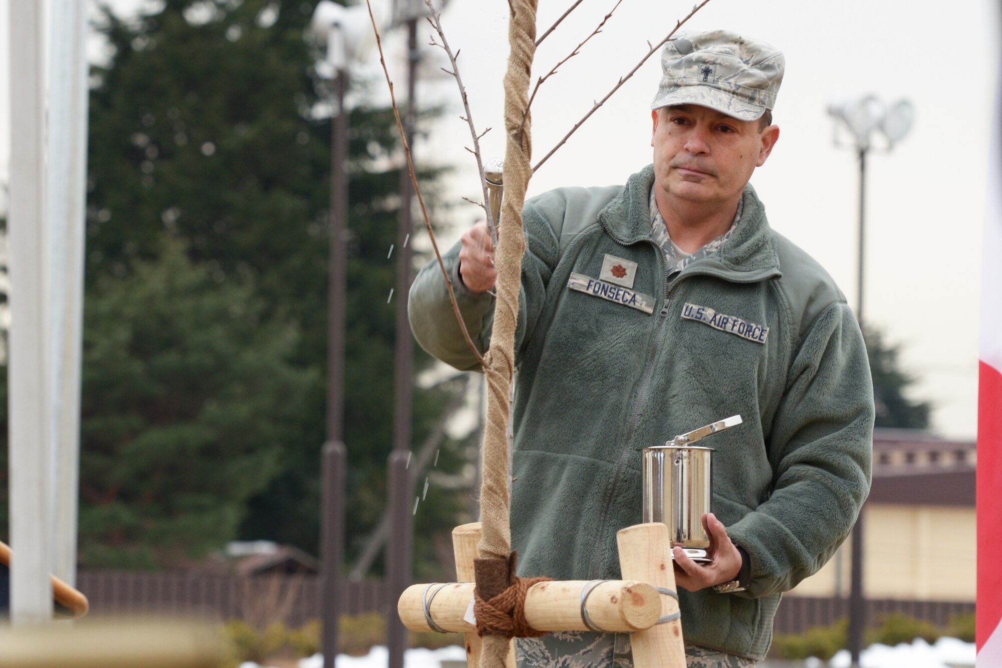 Maj. Oscar Fonseca, 374th Airlift Wing chaplain, splashes holy water onto a Sakura tree during a tree planting ceremony at Yokota Air Base, Japan, Jan. 23, 2016. The water was meant to give the tree good health and bless it to grow well. (U.S. Air Force photo by Staff Sgt. Cody H. Ramirez/Released)