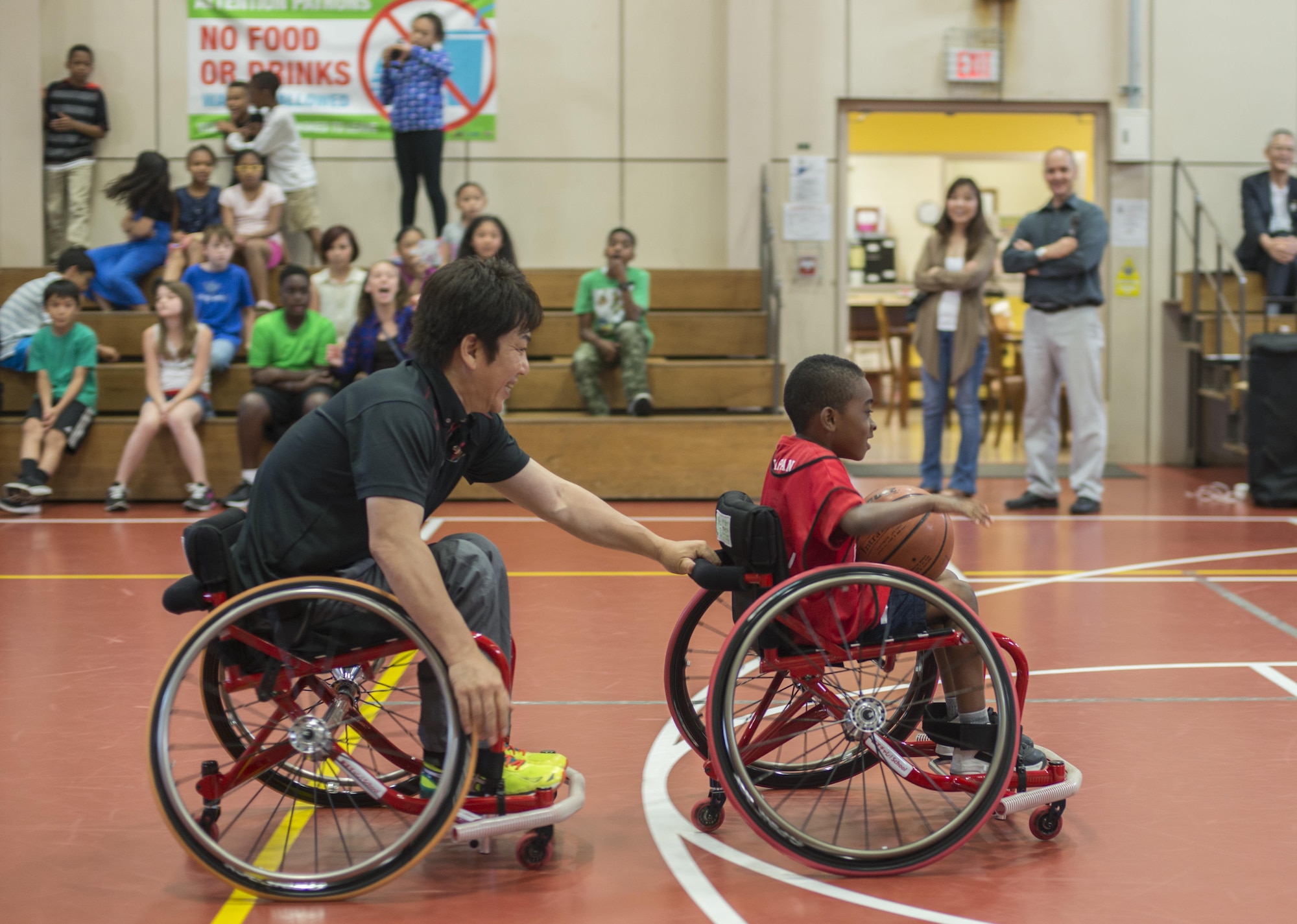 Shinji Negi, a project director with the Nippon Foundation Paralympic Support Center, helps a child at the Lunney Youth Center race to the basketball hoop at Misawa Air Base, Japan, June 28, 2016. Negi travels across the world in order to teach children about life with disabilities and persevering despite difficulties that may occur in life. He was paralyzed from the waist down in high school and went on to become the captain of the Japan Men's National Wheelchair Basketball Team at the 2000 Sydney Paralympic Games. (U.S. Air Force photo by Senior Airman Brittany A. Chase)