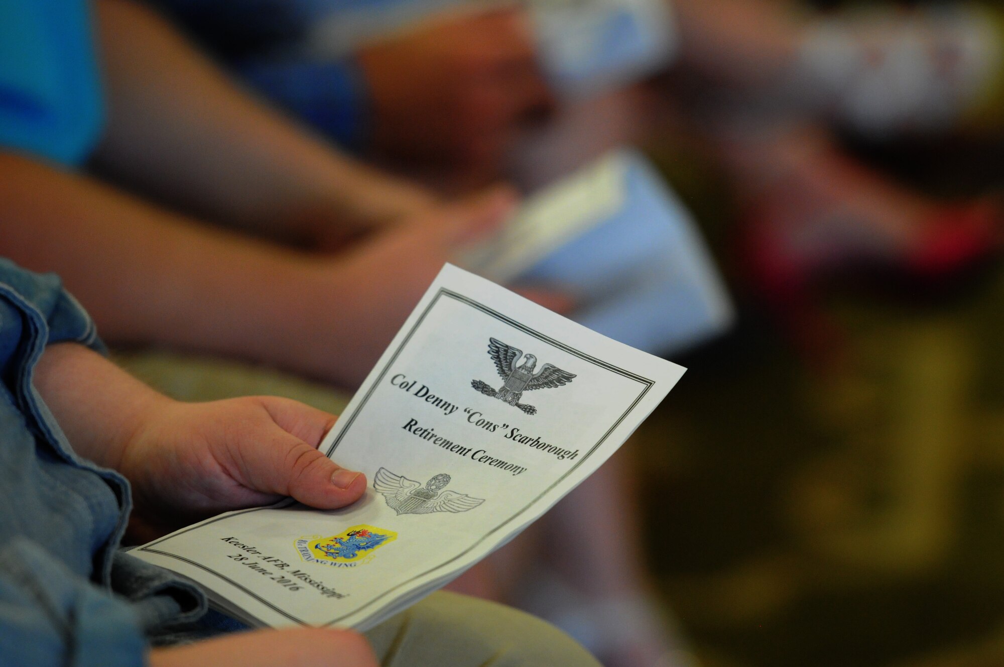 An event program is held by an attendee during the retirement ceremony for Col. Dennis Scarborough, 81st Training Wing vice commander, at the Bay Breeze Event Center June 28, 2016, on Keesler Air Force Base, Miss. Scarborough retired with 27 years of military service. He has served multiple tours as an F-15C instructor and evaluator and has held positions in the fields of defense policy, operational plans, safety and aircraft maintenance. He has commanded at the squadron level and served as an operations group deputy commander. (U.S. Air Force photo by Kemberly Groue/Released)