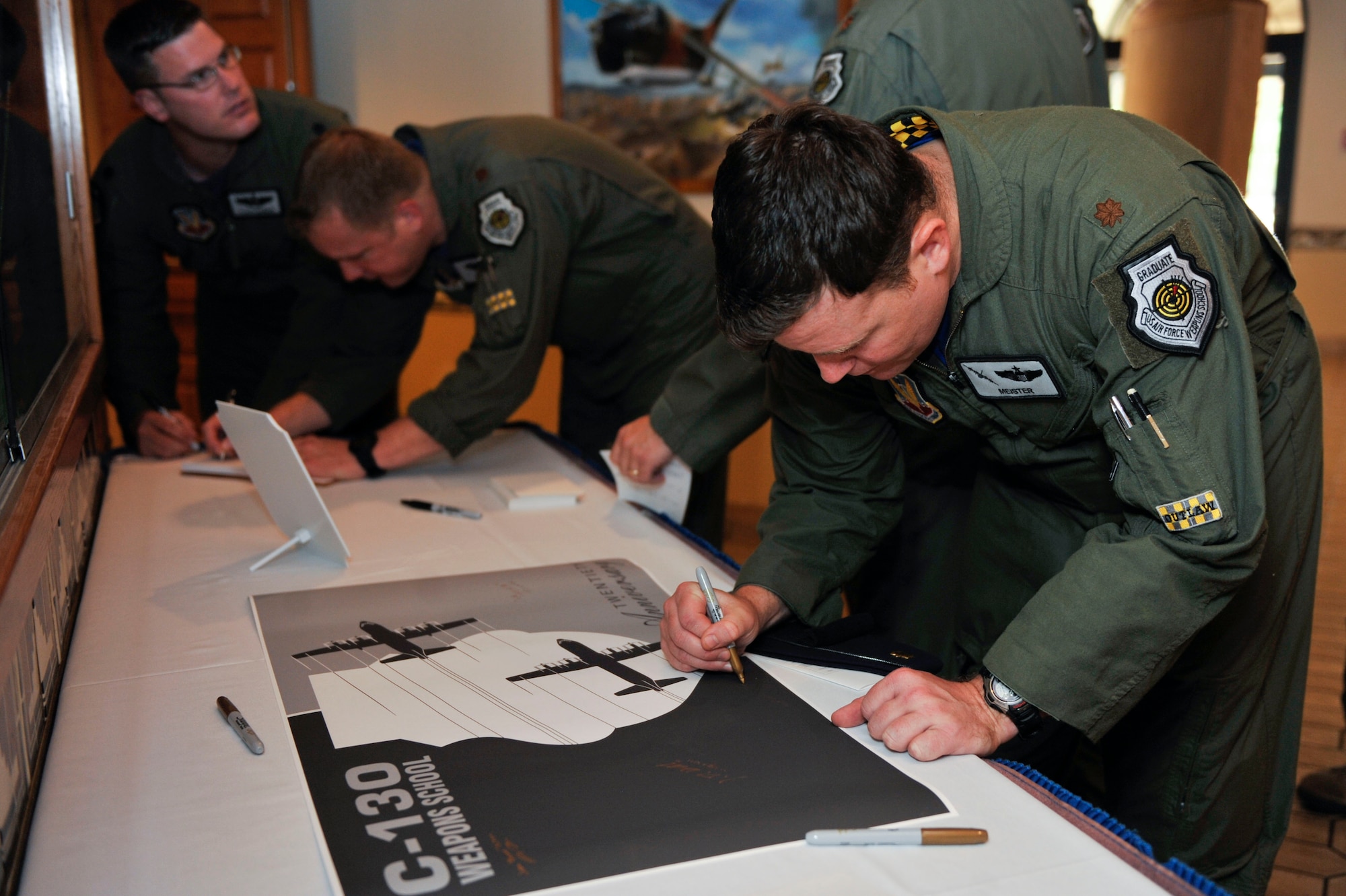 U.S. Air Force personnel from the C-130 Weapons Instructor Course sign a memento celebrating the 20-year anniversary of the C-130 WIC, June, 24, 2016, at Nellis Air Force Base, Nev. Throughout the years, the WIC has moved from Air Combat Command to Air Mobility Command and back to ACC. (U.S. Air Force photo by Senior Airman Stephanie Serrano) 