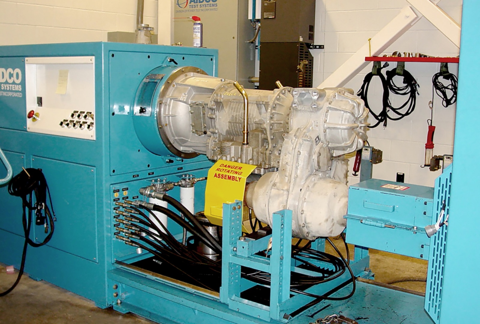 Shown is an AIDCO model 450 transmission dynamometer installed at the Ohio Army National Guard’s Combined Support Maintenance Shop on Defense Supply Center Columbus. To run the test the transmission subassembly is mounted on the dynamometer and a short lever allows technicians to manually shift gears between park, reverse neutral and drive. Other connections allow control and data signals to pass between the control console and the transmission.