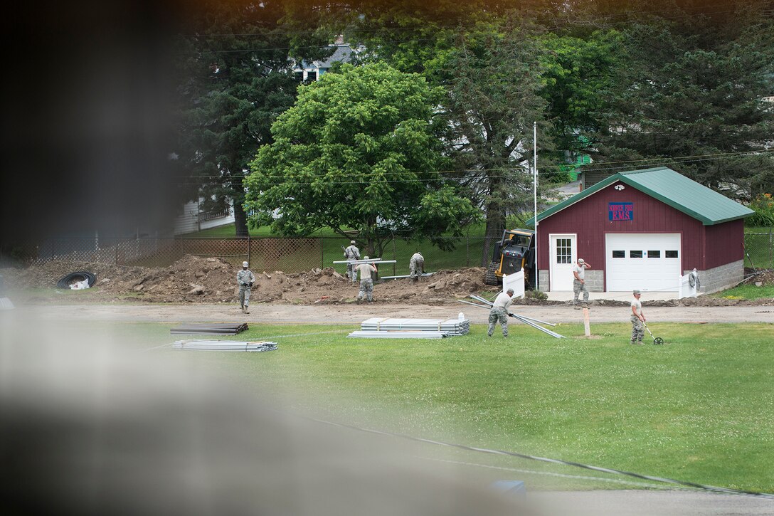 Seen through the side of the grand stand at the Chenango County Fairgrounds, Airmen from the 307th Civil Engineering Squadron (CES) work to install new water, plumbing and electrical lines on June 29, 2016, Norwich, N.Y. The 307th CES is an Air Force Reserve squadron assigned under the 307th Bomb Wing at Barksdale Air Force Base, La., and is in Norwich to participate in a community restoration project in support of the Innovative Readiness Training Program.  (U.S. Air Force photo by Master Sgt. Greg Steele/Released)