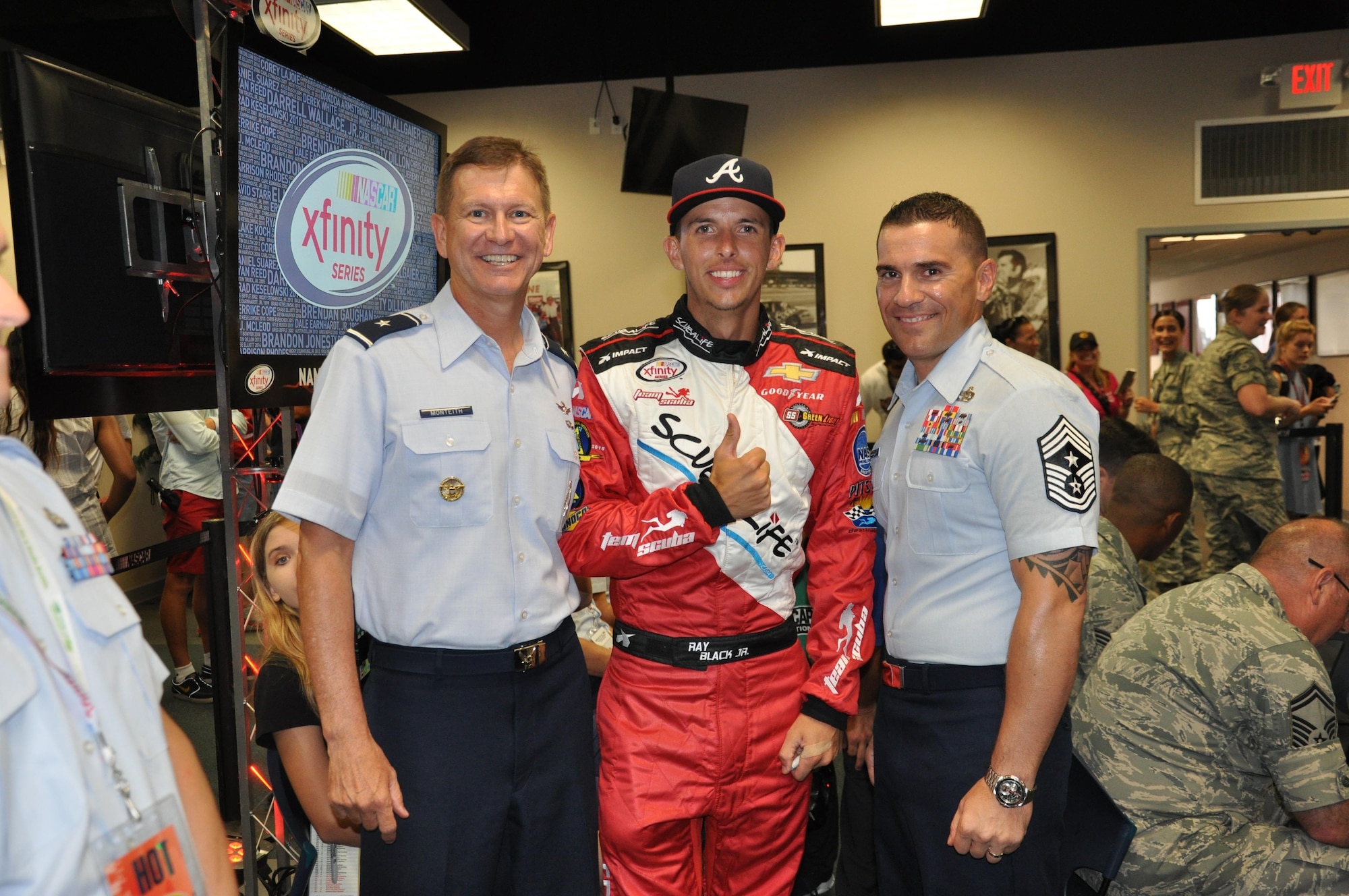 Brig. Gen. Wayne Monteith, 45th Space Wing commander, left, and Chief Master Sgt. Jason Lamoureux, 45th SW command chief, pose for a photo with NASCAR driver Ray Black Jr. at the NASCAR Drivers and Crew Chiefs meeting at Daytona International Speedway July 1, 2016. NASCAR driver Ray Black Jr. from SS Green Light Racing supported the wing by displaying the 45th Space Wing name across the windshield of his Chevrolet Camaro No. 07 racecar during the race instead of the typical Xfinity logo that is displayed for Xfinity races. (U.S. Air Force photo by 1st Lt. Alicia Premo/Released)