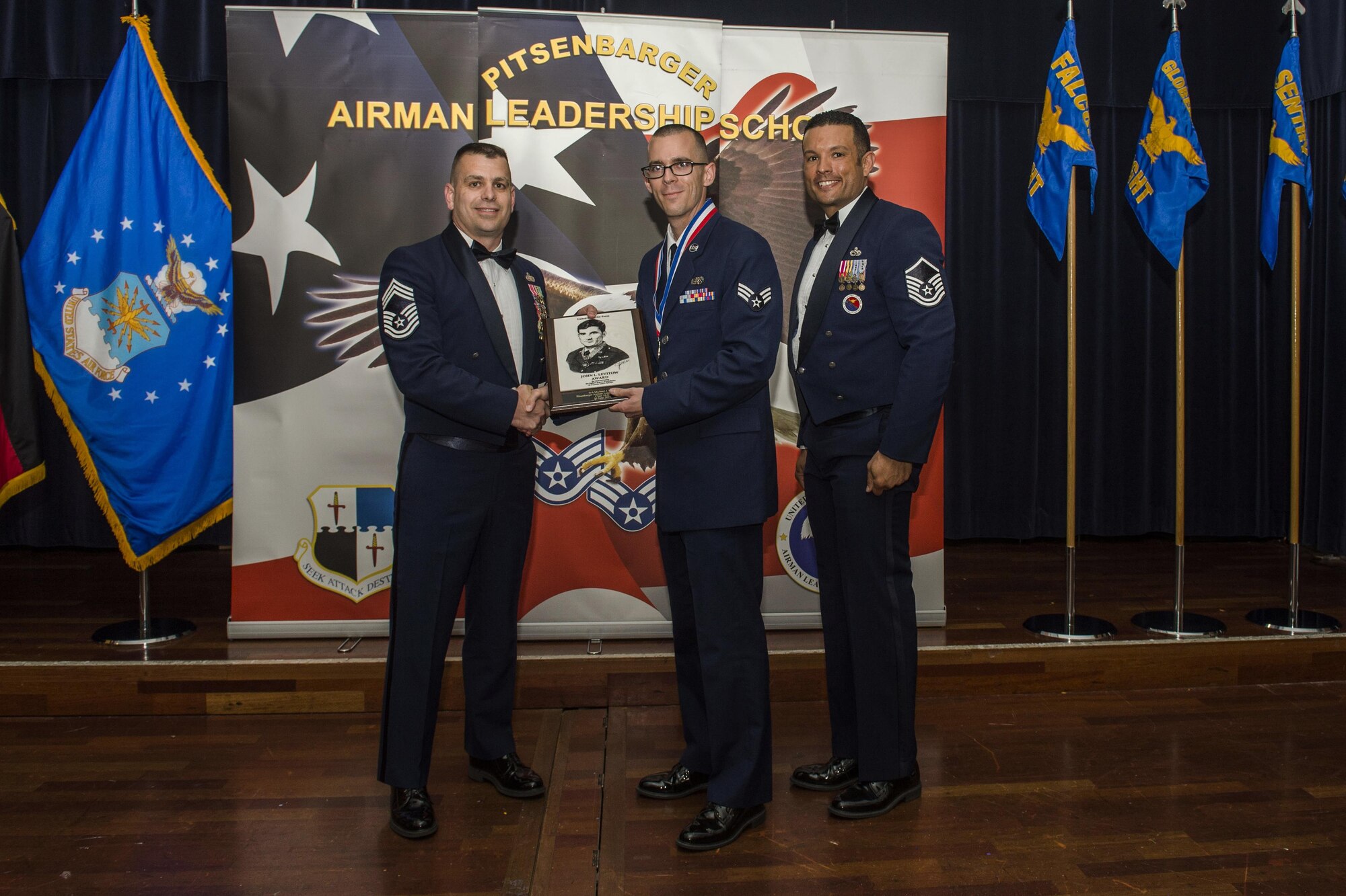 U.S. Air Force Senior Airman Michael Kent, a 726 Air Mobility Squadron client systems technician, middle, receives the John L. Levitow during the Pitsenbarger Airman Leadership School 16-E graduation at Club Eifel on Spangdahlem Air Base, Germany, June 30, 2016. The Levitow award is highest honor given to the student who displays excellence in all categories of ALS. (U.S. Air Force photo by Senior Airman Luke Kitterman/Released)