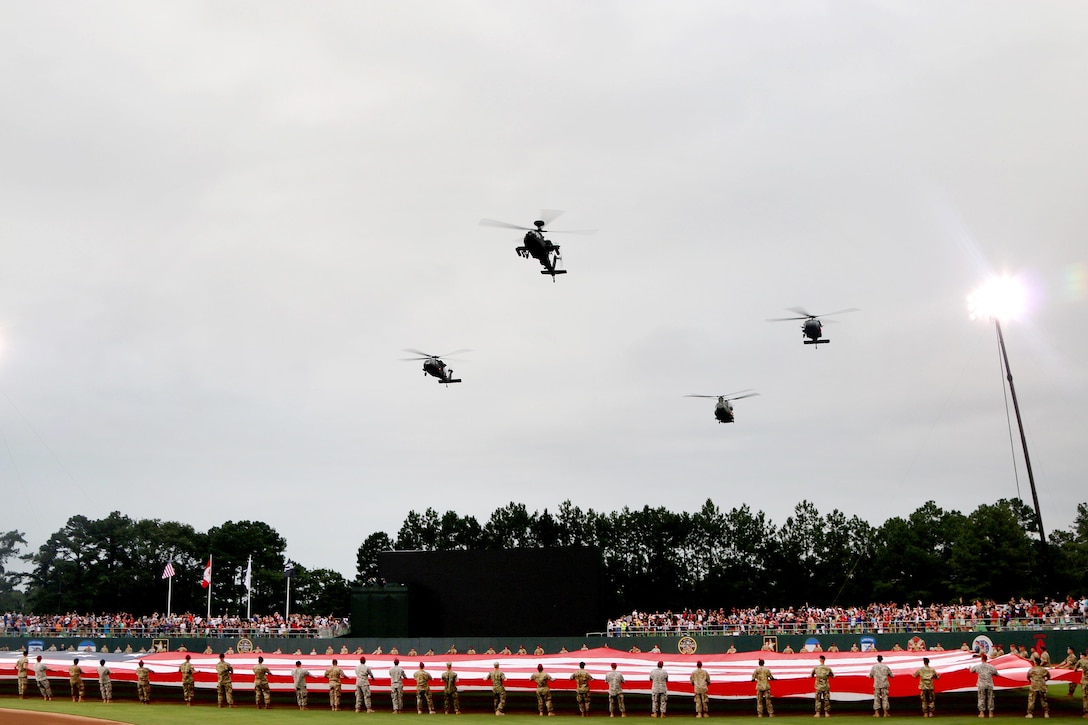 AH-64 Apache, UH-60 Black Hawk and CH-47 Chinook helicopters fly over Fort Bragg Field while soldiers display the U.S. flag and Army Staff Sgt. Traci Gregg sings the national anthem before the start of the baseball game between the Florida Marlins and Atlanta Braves at Fort Bragg, N.C., July 3, 2016. Army photo by Staff Sgt. Jason Duhr