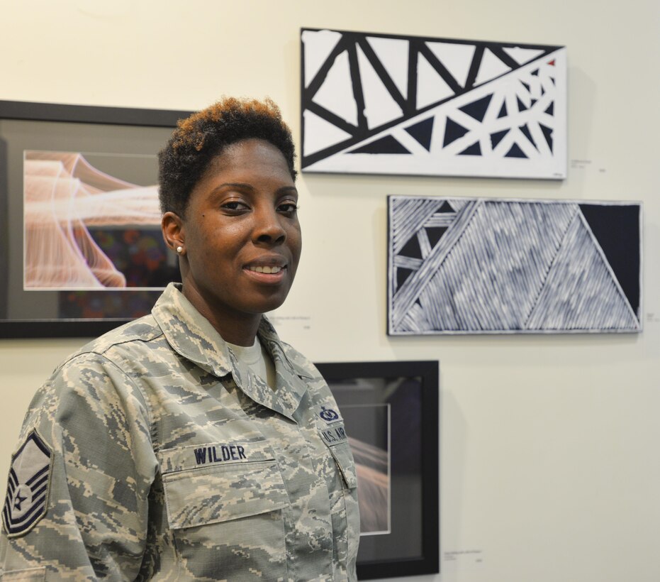 Air Force Master Sgt. Bahiya Wilder, 60th Operations Support Squadron aircrew flight equipment quality assurance flight chief, stands with two of her paintings on display at the Solano Town Center Mall in Fairfield, Calif., June 22, 2016. Air Force photo by Senior Airman Amber Carter