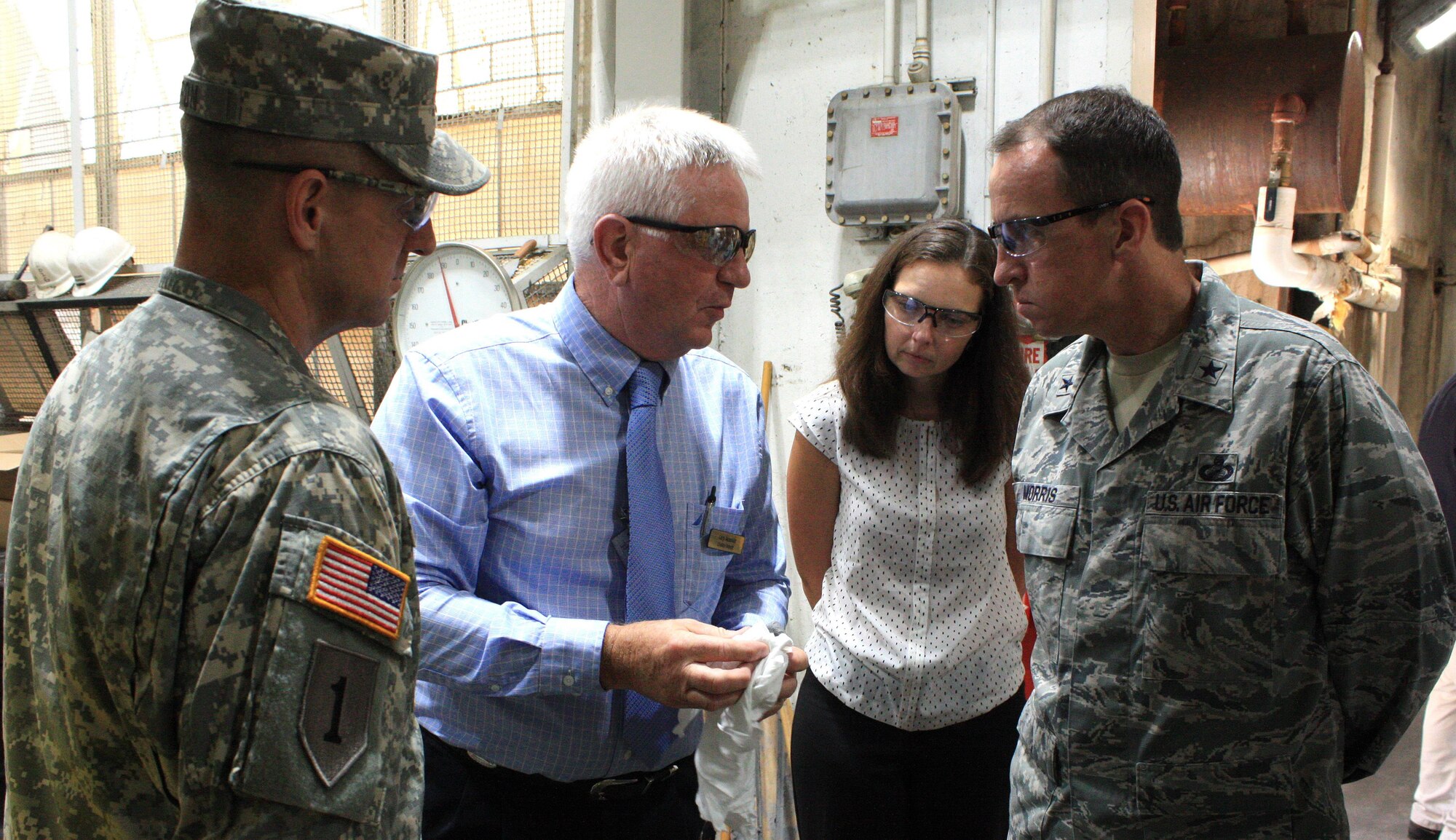 Gary Reasnor (second from left), civilian deputy to the commander at McAlester Army Ammunition Plant, Okla., tells Air Force Brig. Gen. Shaun Morris (far right), Program Executive Office for Weapons, Eglin Air Force Base, Fla., and Casey Sadler, the plastic bonded explosive used to fill Air Force penetrator bombs. (Photo Credit: Kevin Jackson (AMC))