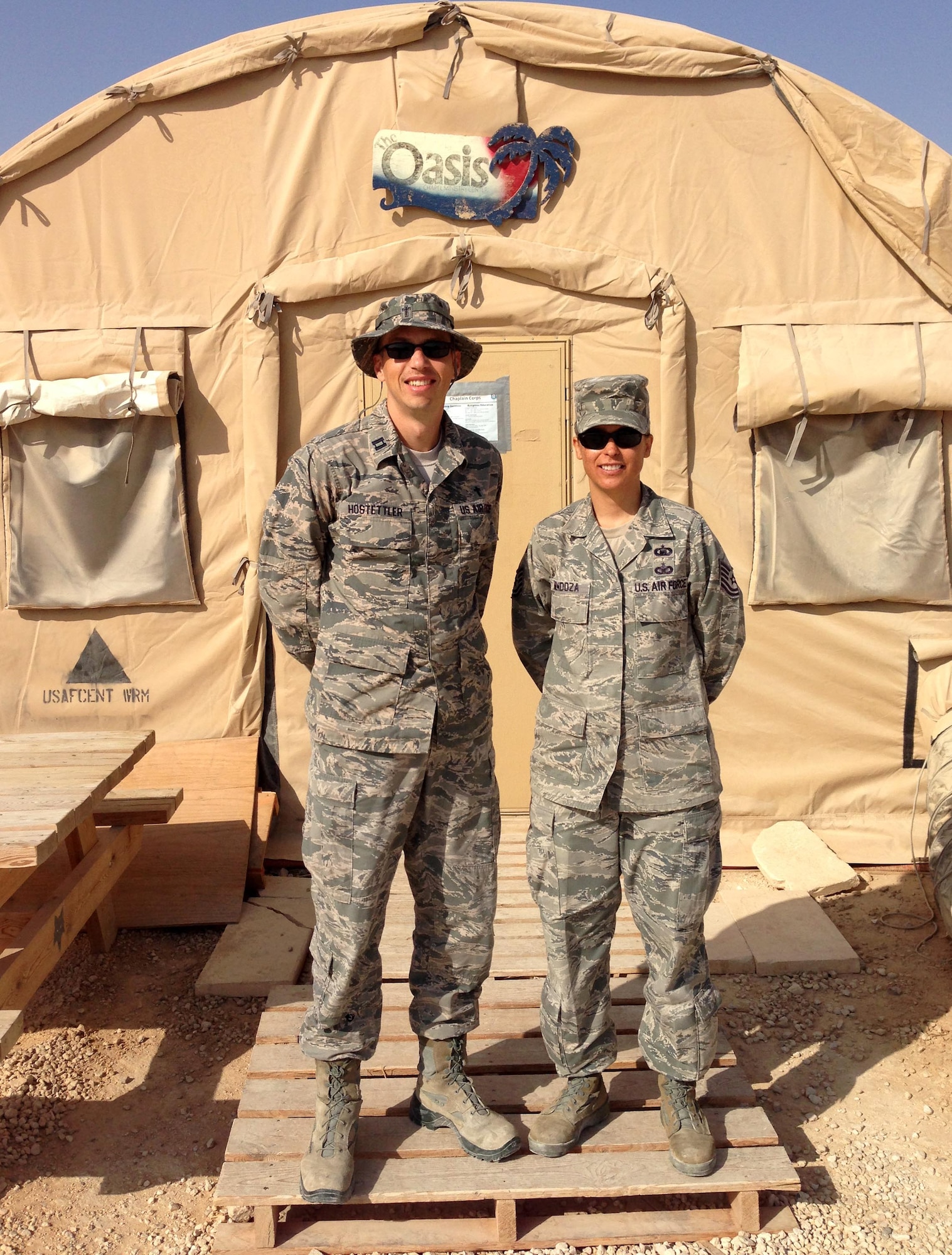 U.S. Air Force Capt. Kevin Hostettler, a 35th Fighter Wing chaplain, and then Tech. Sgt. Stenya Mendoza, a 35th FW chaplain assistant, stand in front of “The Oasis,” an Airman's Ministry Center during their deployment to Southwest Asia, June 28, 2015.  Mendoza ran the quiet center, an alternative to the local recreation center, which offered free goods including daily care packages aid deployed members. (U.S. Air Force courtesy photo)