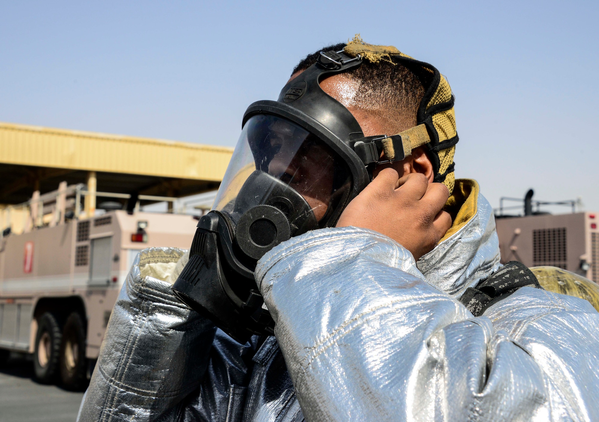 Senior Airman Dashawn Gilford, 379th Expeditionary Civil Engineer Squadron firefighter, dons his self-contained breathing apparatus face piece prior to operating a hand line from Engine 21 June 24, 2016, at Al Udeid Air Base, Qatar. There is more than one fire station here to provide adequate coverage and quick response time based on the geography of the base and volume of calls. (U.S. Air Force photo/Senior Airman Janelle Patiño/Released)